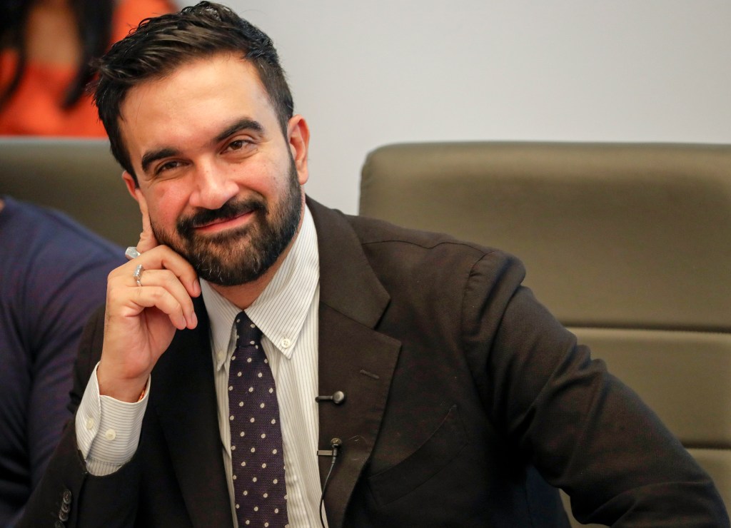 Zohran Mamdani smiling at a town hall Q&A.