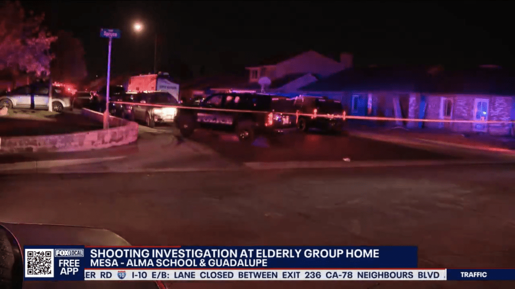 Crime scene at an elderly group home with flashing police lights, an ambulance, and yellow police tape at night.