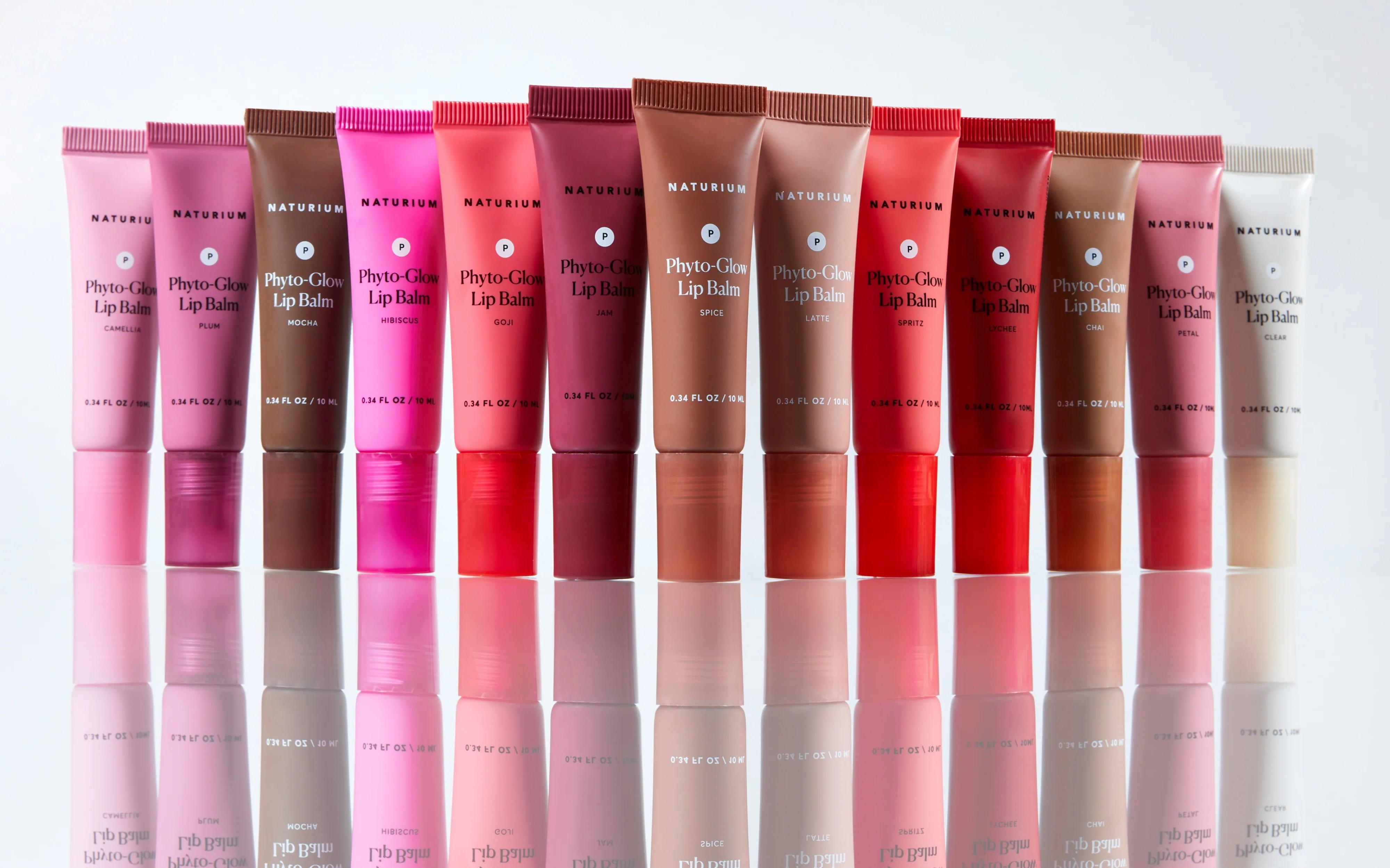 A group of 13 Naturium Phyto-Glow lip balms arranged in a line.