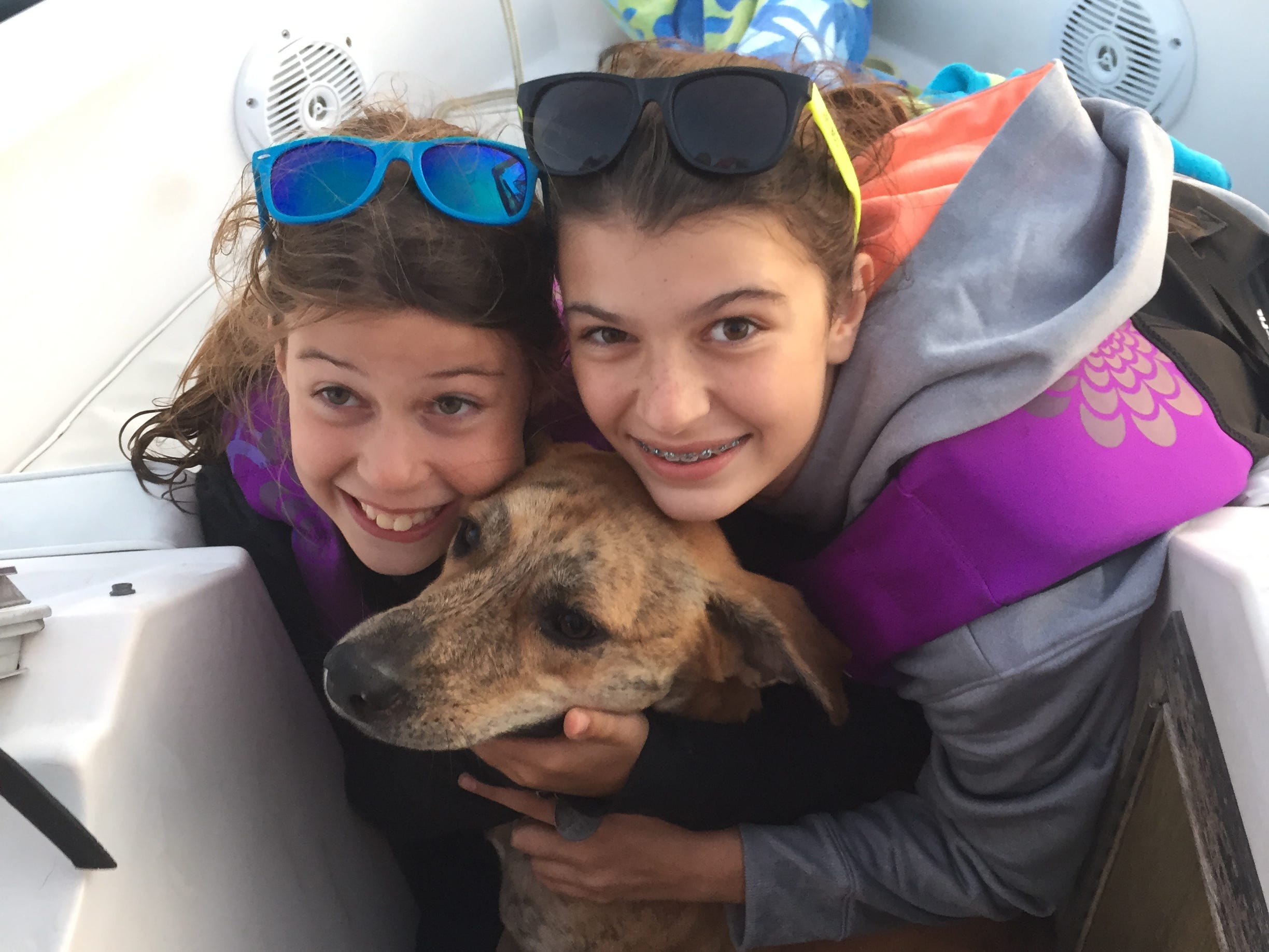 The author and her sister hugging a dog on a boat.