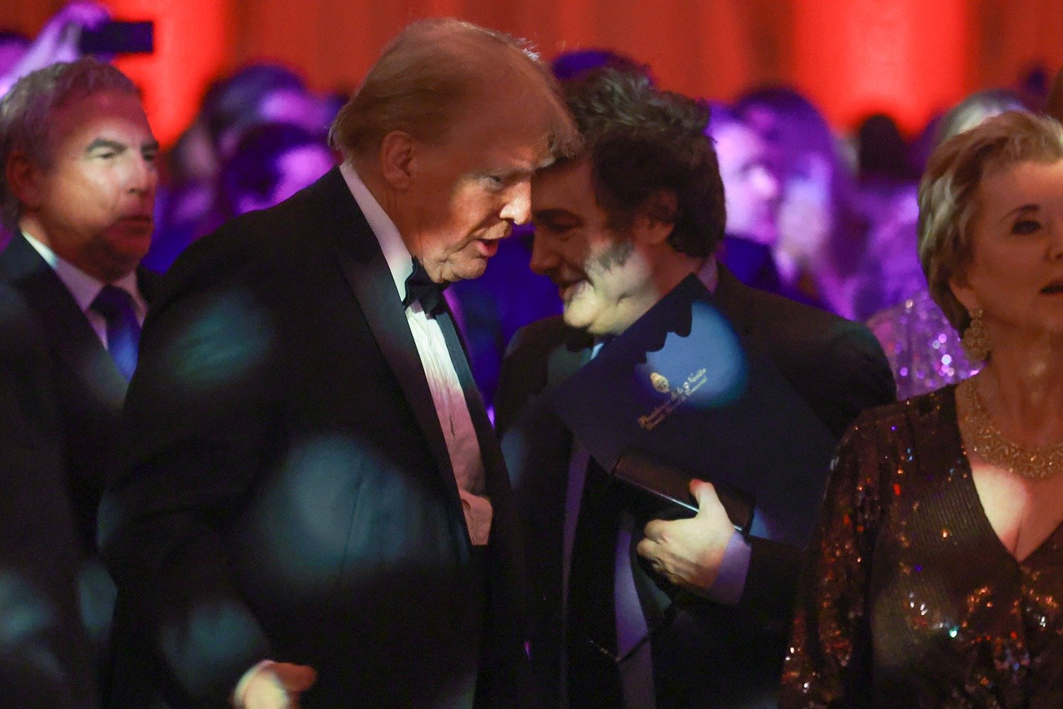 Donald Trump and Javier Milei, both wearing suits, talk to each other in a crowded room.