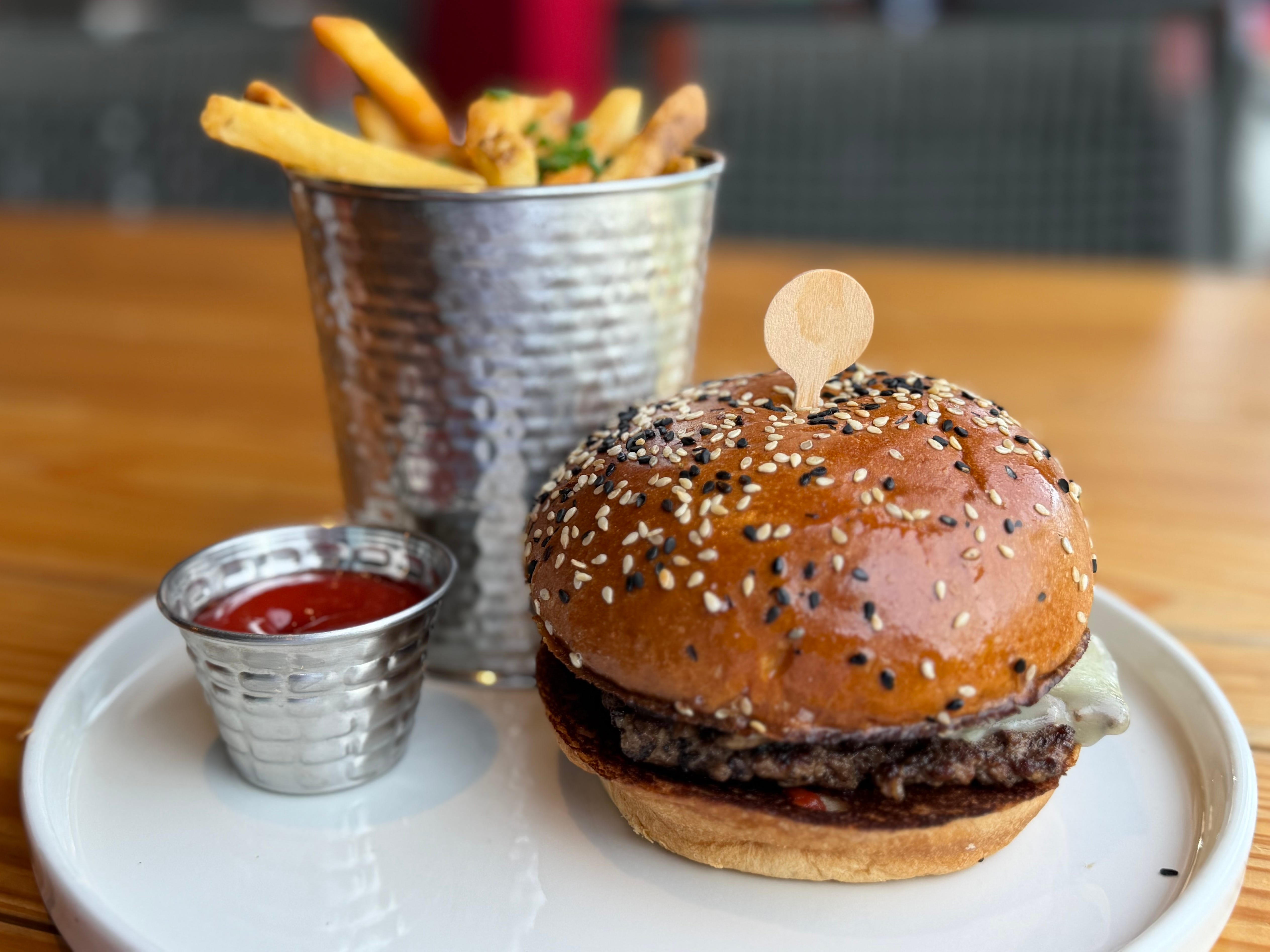 A plate with a burger, a cup of fries, and a side of ketchup on a plate at Gordon Ramsay Burger.