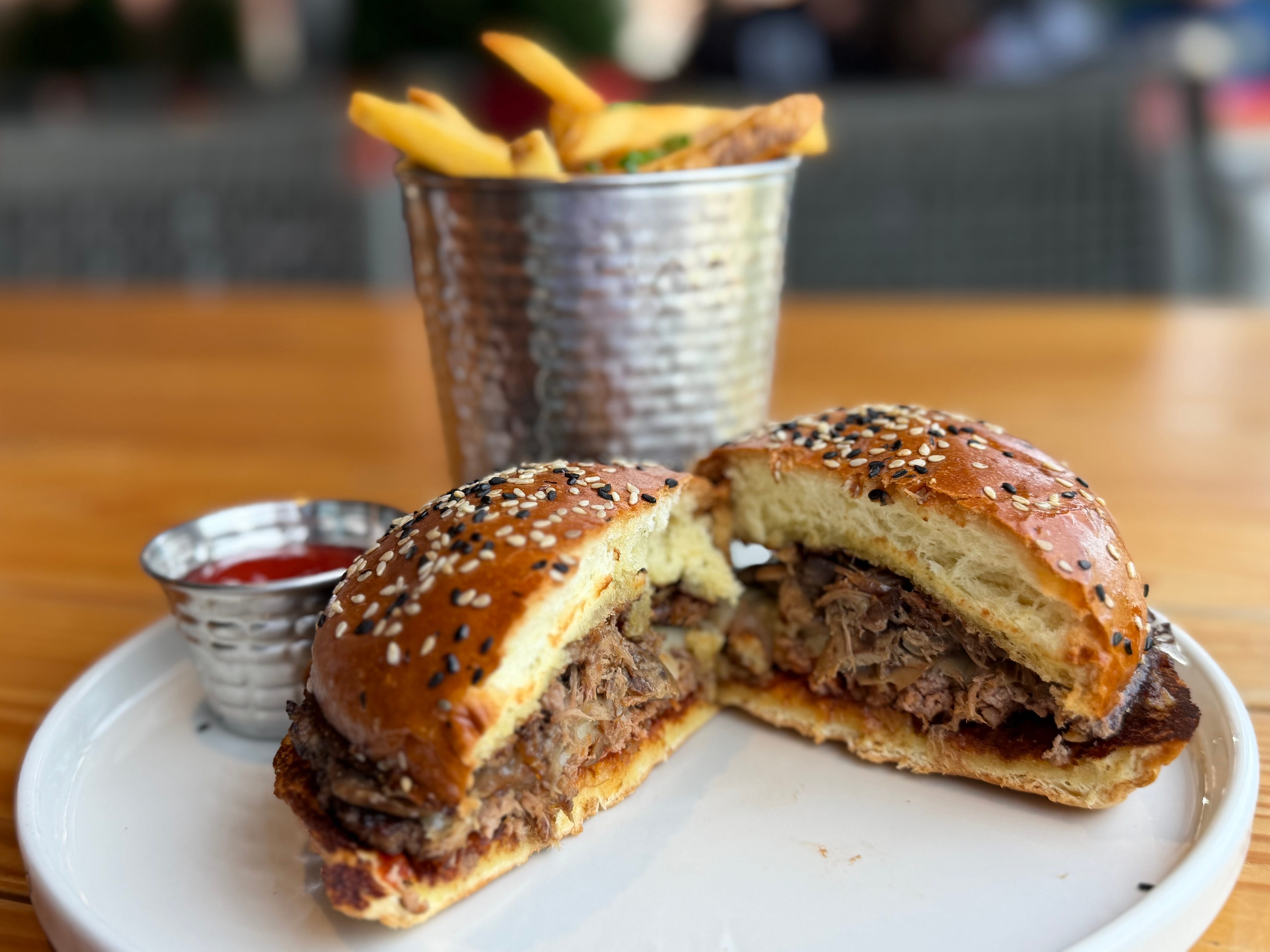 A burger cut open in half on a plate with a cup of fries and a side of ketchup.