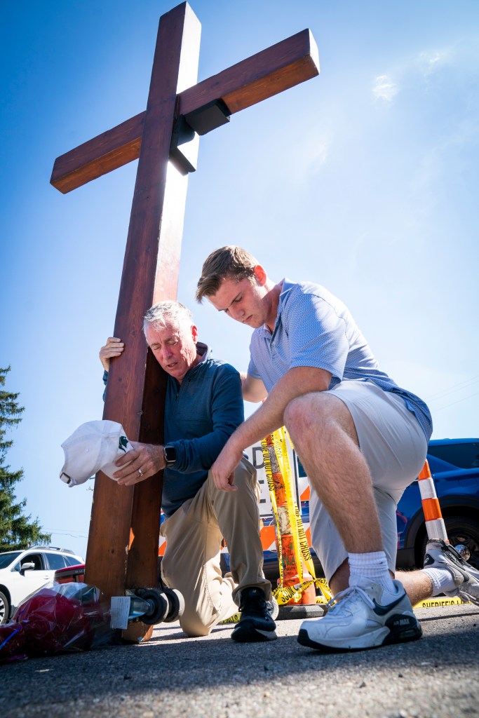 Dan Beazley and Benjamin Stanley pray after Beazley carried a cross he made to a police barrier near the site of a church shooting.