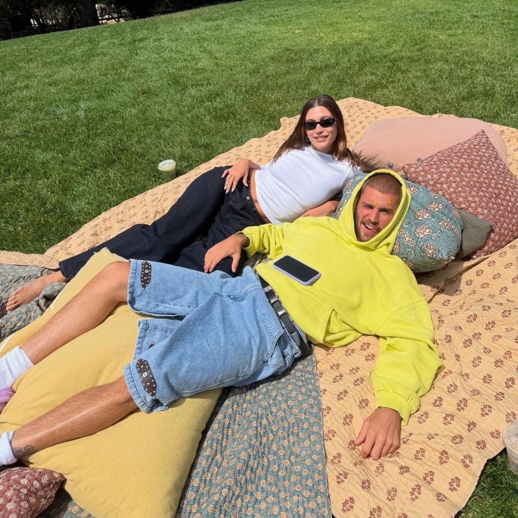 Hailey and Justin Bieber lying on a picnic blanket on grass.
