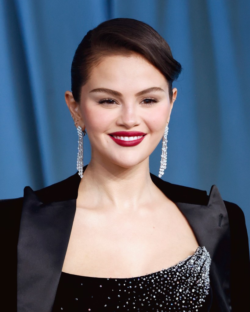 Selena Gomez smiles, wearing a black top and jacket, with diamond earrings and dark red lipstick, at the 2025 Academy Museum Gala.