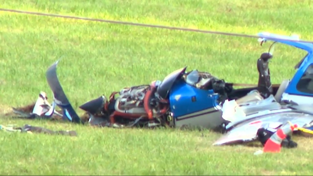 Wreckage of a small blue and white plane on a grassy field.