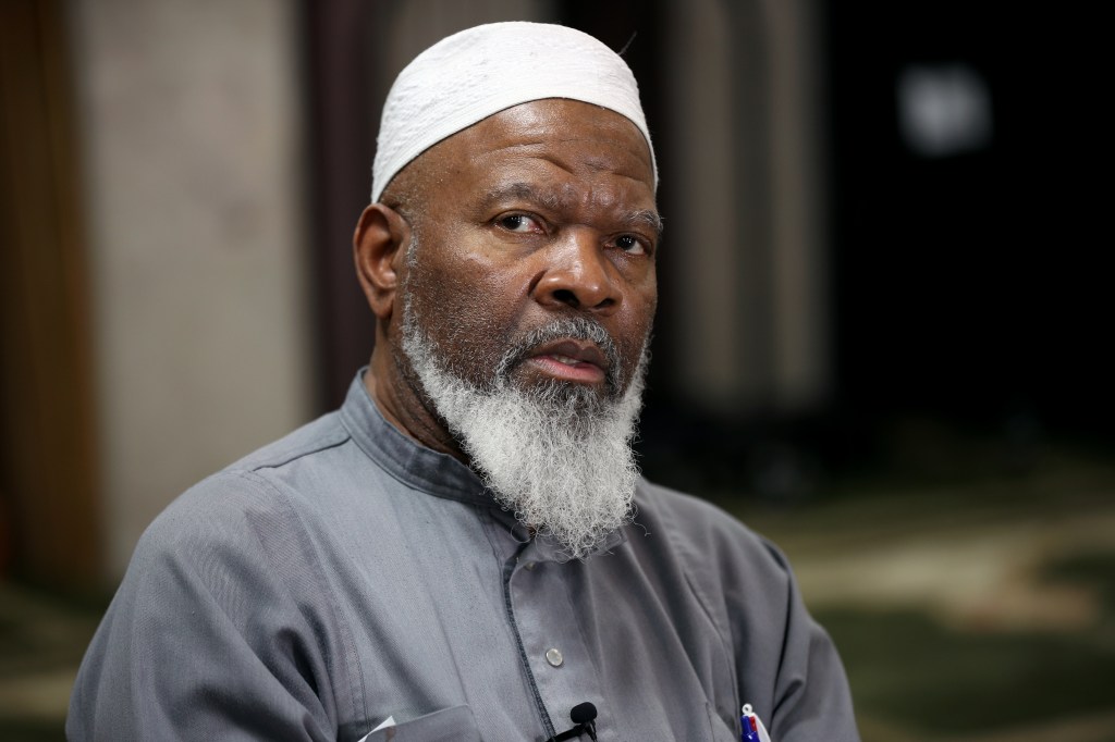 Imam Siraj Wahhaj, founder of Masjid At-Taqwa, wearing a white cap and grey tunic.
