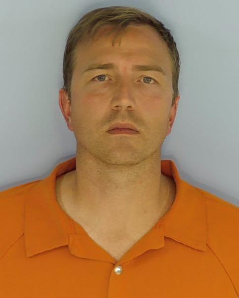 Mugshot of a light-skinned man with short blond hair and blue eyes, wearing an orange shirt.