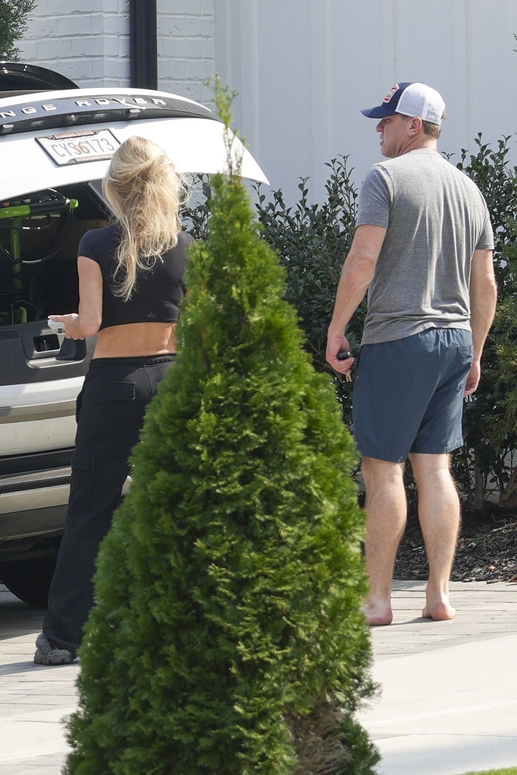 Kim Zolciak and Kyle Mowitz from behind, with Kim looking into the open trunk of a white Range Rover and Kyle standing barefoot on a paved area.
