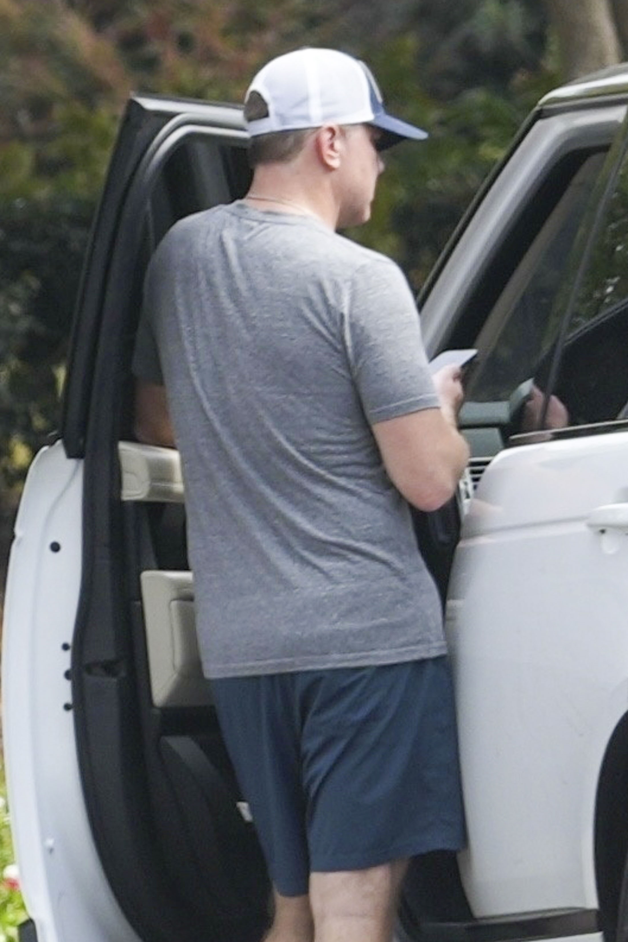 Kyle Mowitz in a gray t-shirt, blue shorts, and a white and blue baseball cap, standing next to an open car door.