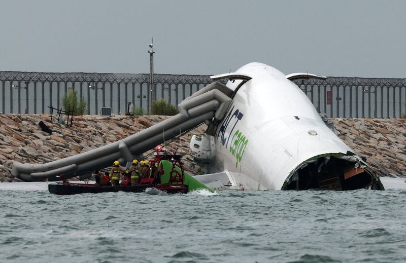 Emergency personnel work near a cargo plane lying partially in the sea after it veered off the runway during landing at Hong Kong International Airport in Hong Kong, China, October 20, 2025.