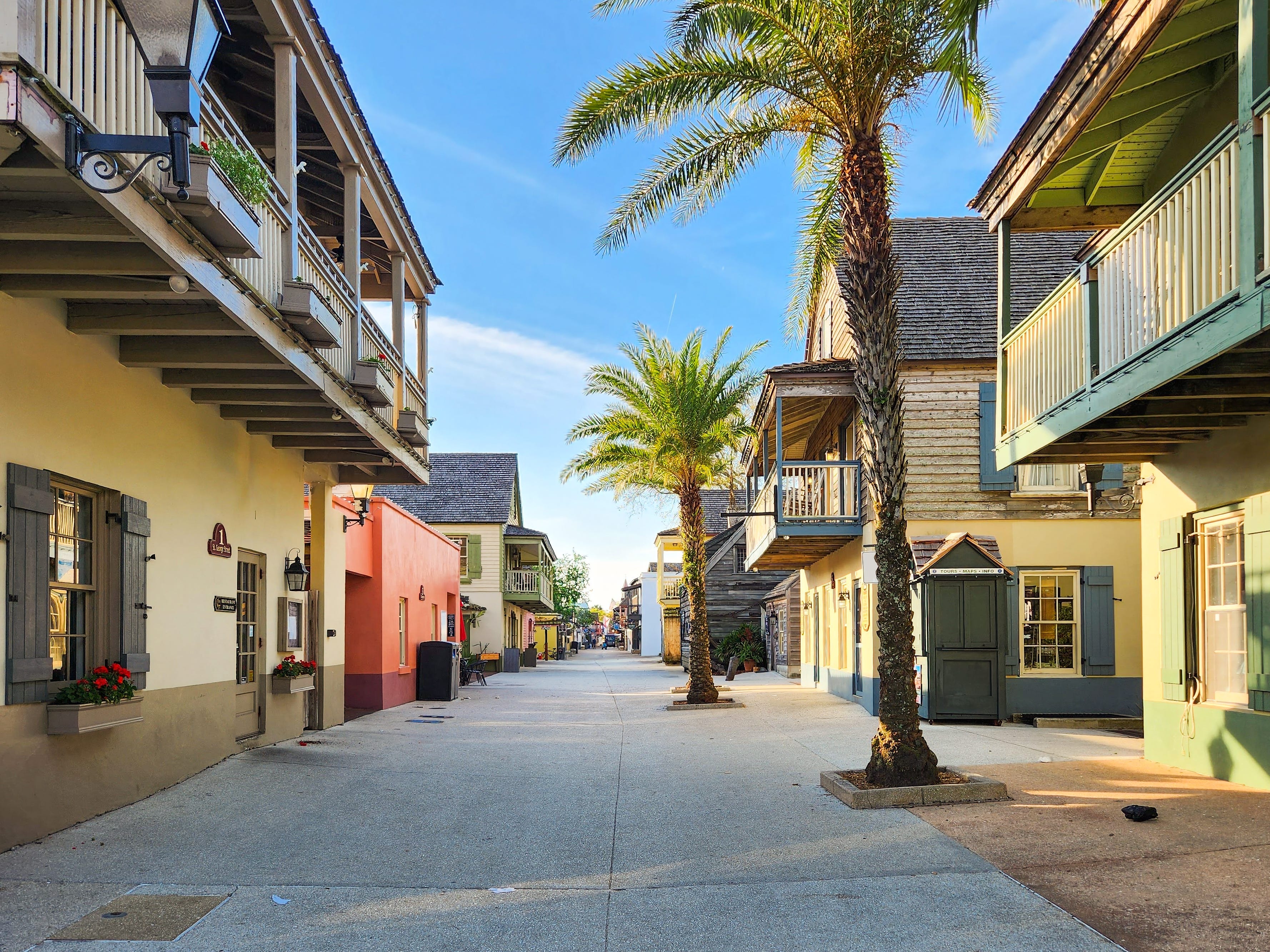 A walkway surrounded by charming two-story buildings and palm trees.