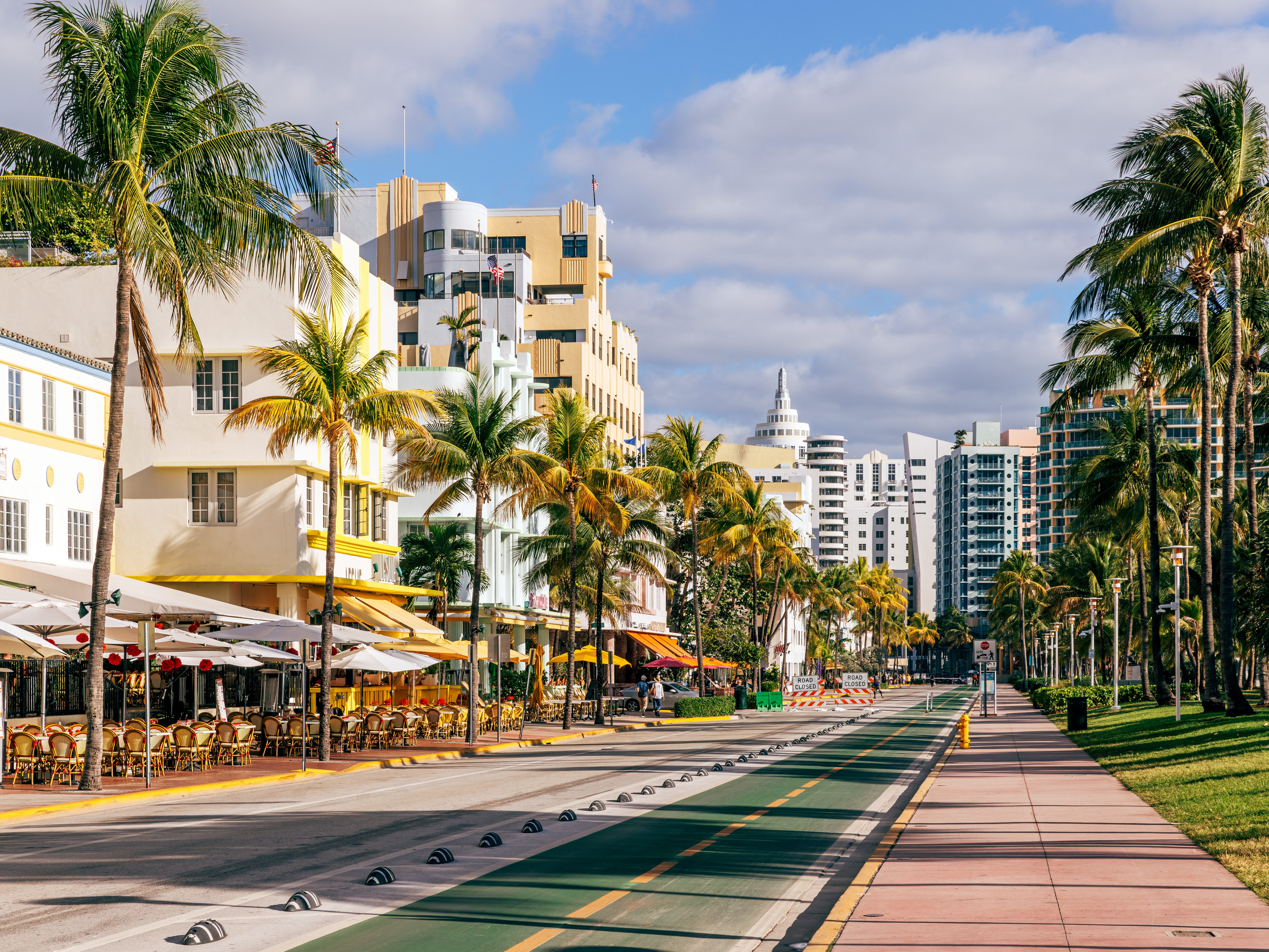 A street lined with Art Deco buildings, restaurants, and palm trees in Miami.