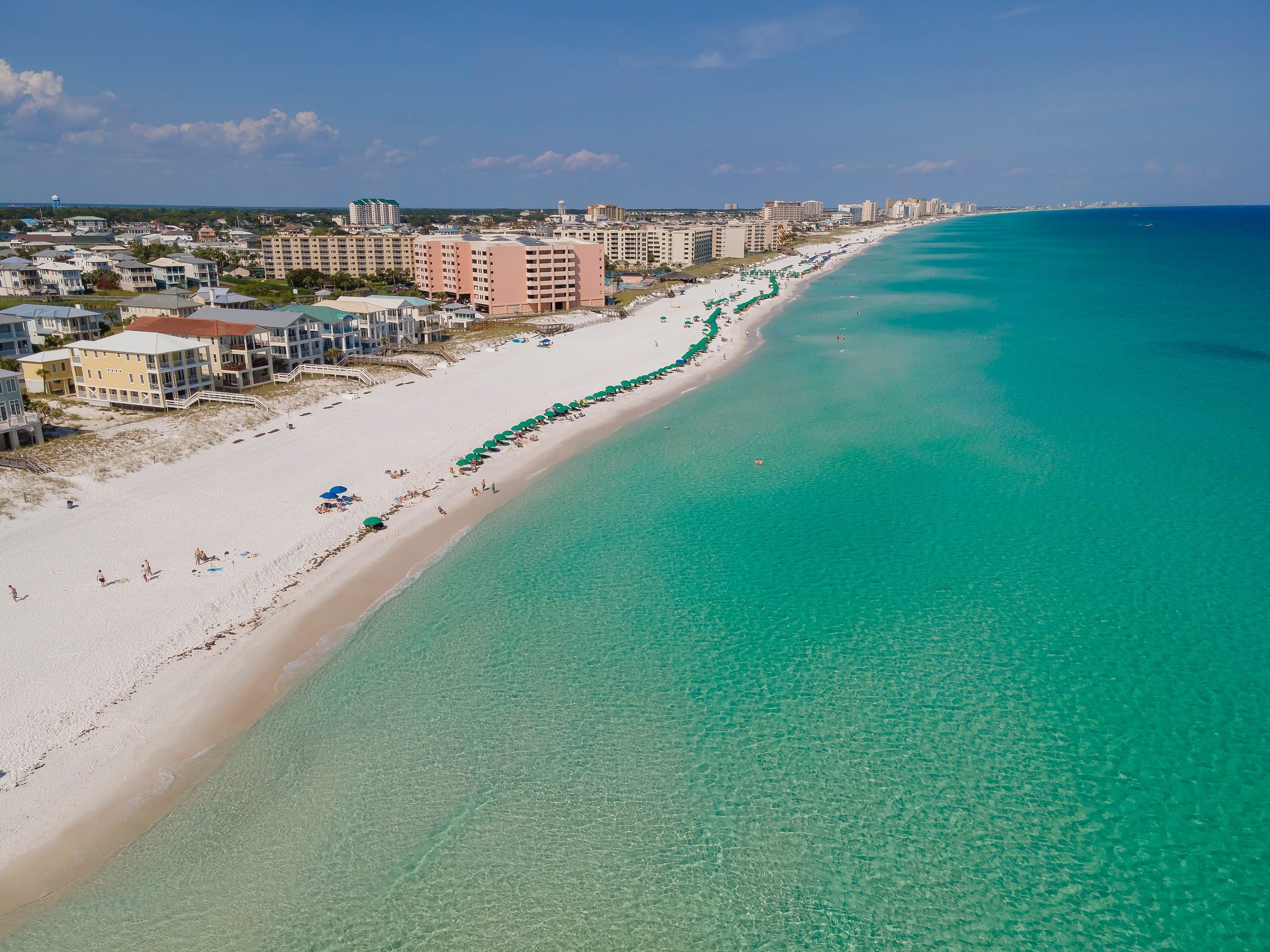 An aerial view of a city along a white-sand beach with bright blue water.