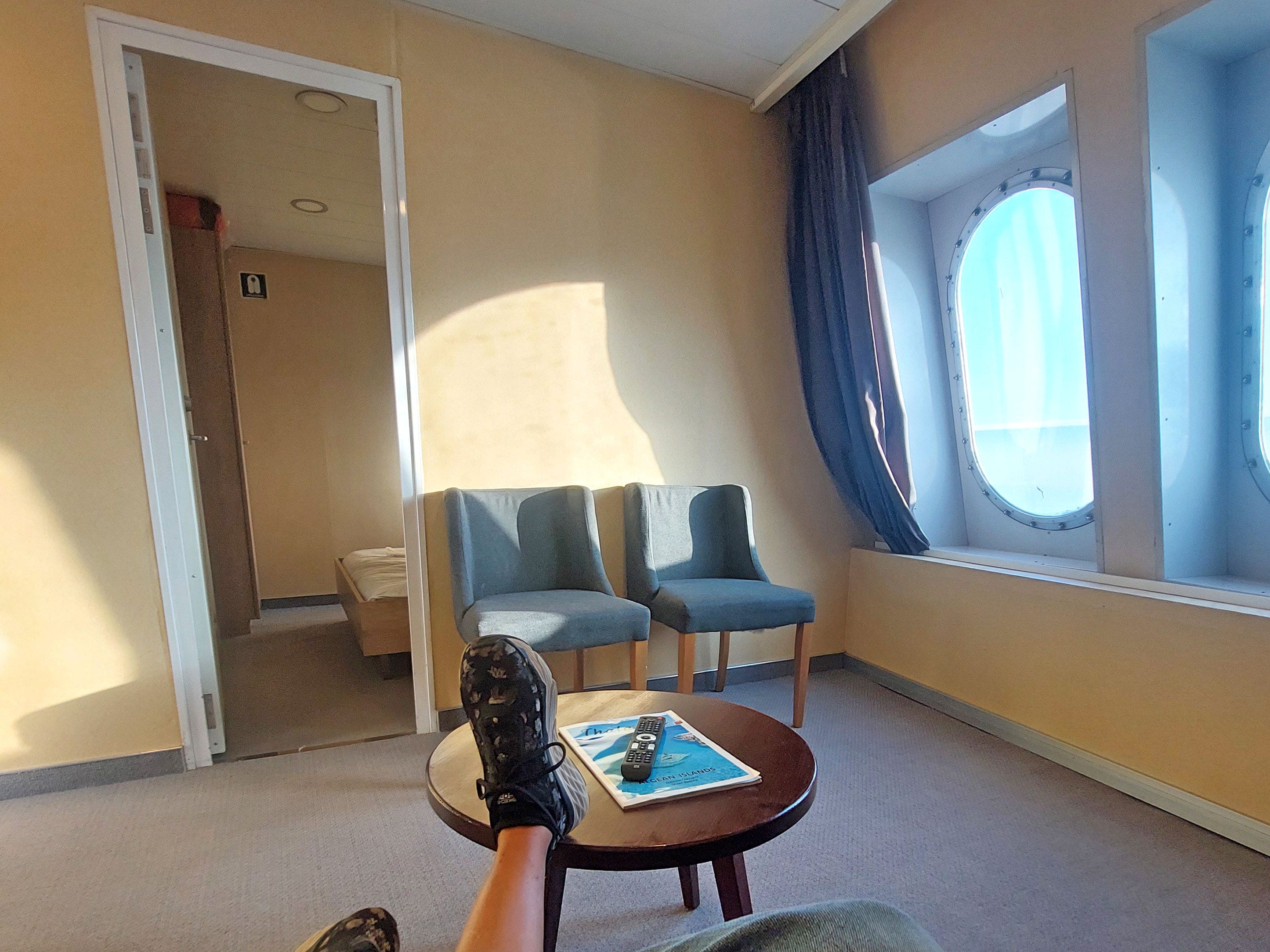 A spacious living room on a boat with chairs, a table, large windows, and a door to another room.