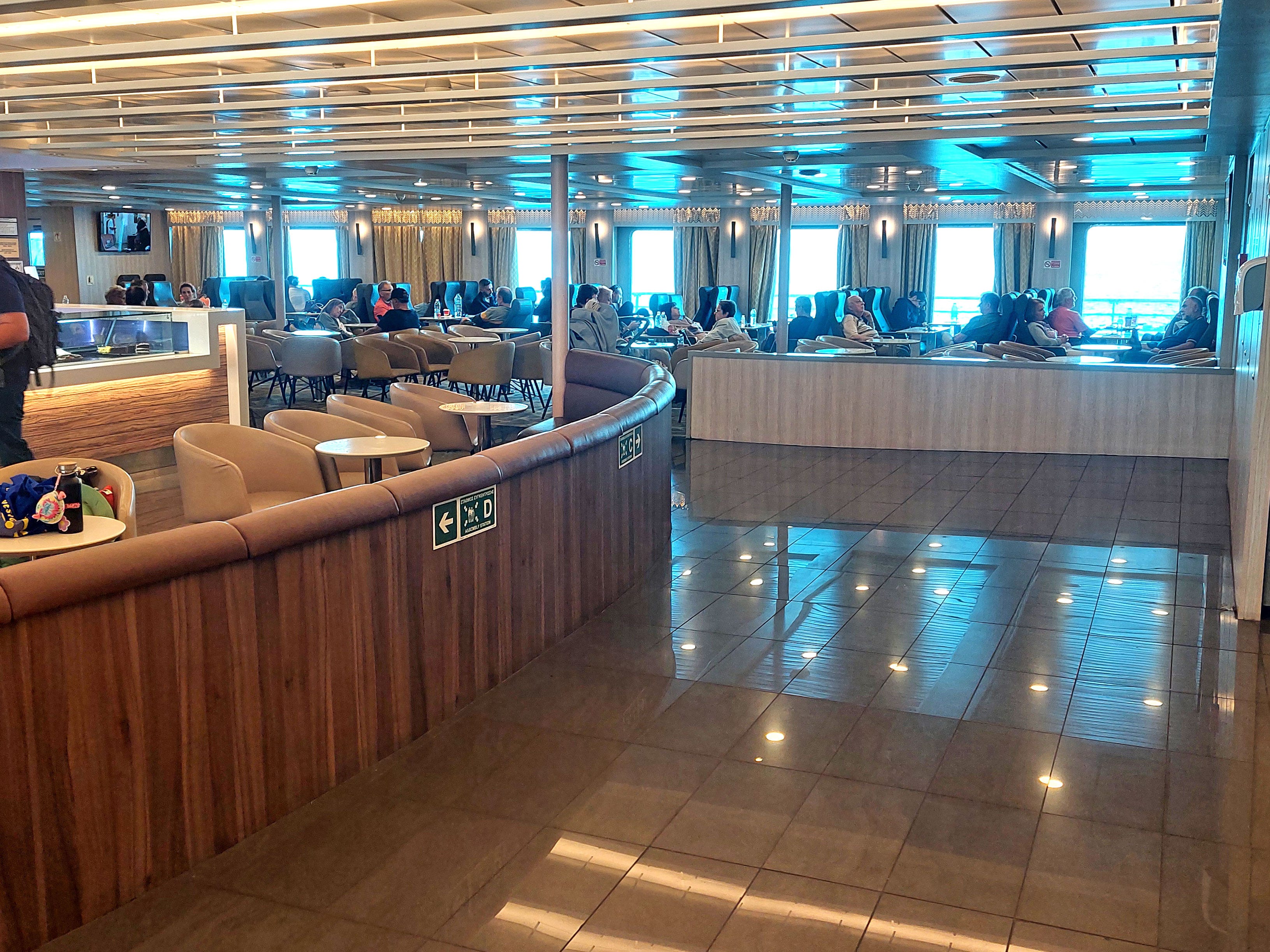 The interior of a ferry with airplane-style seating and tables with chairs.
