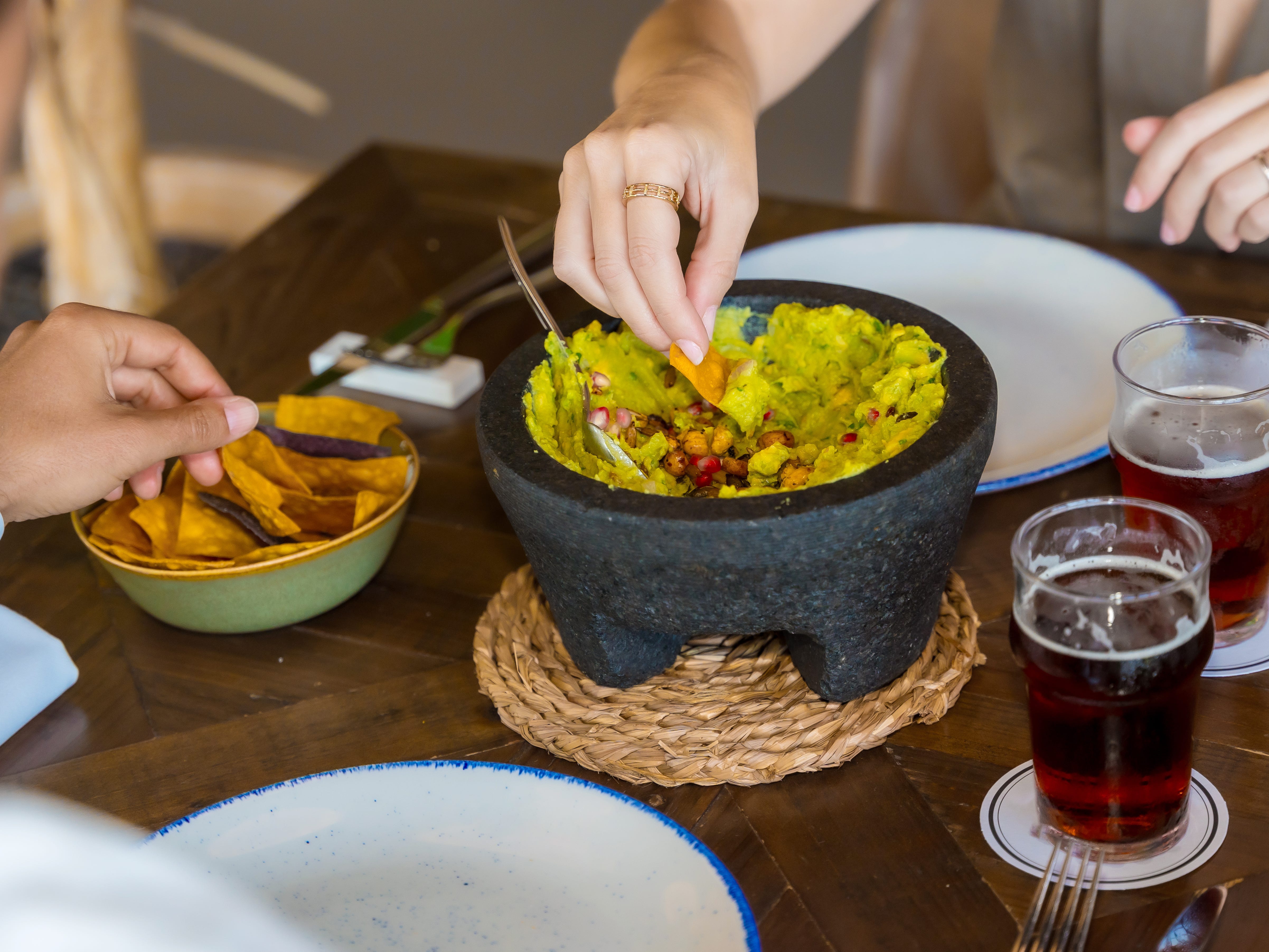Hands of two diners sharing a bowl of guacamole at a Mexican restaurant.
