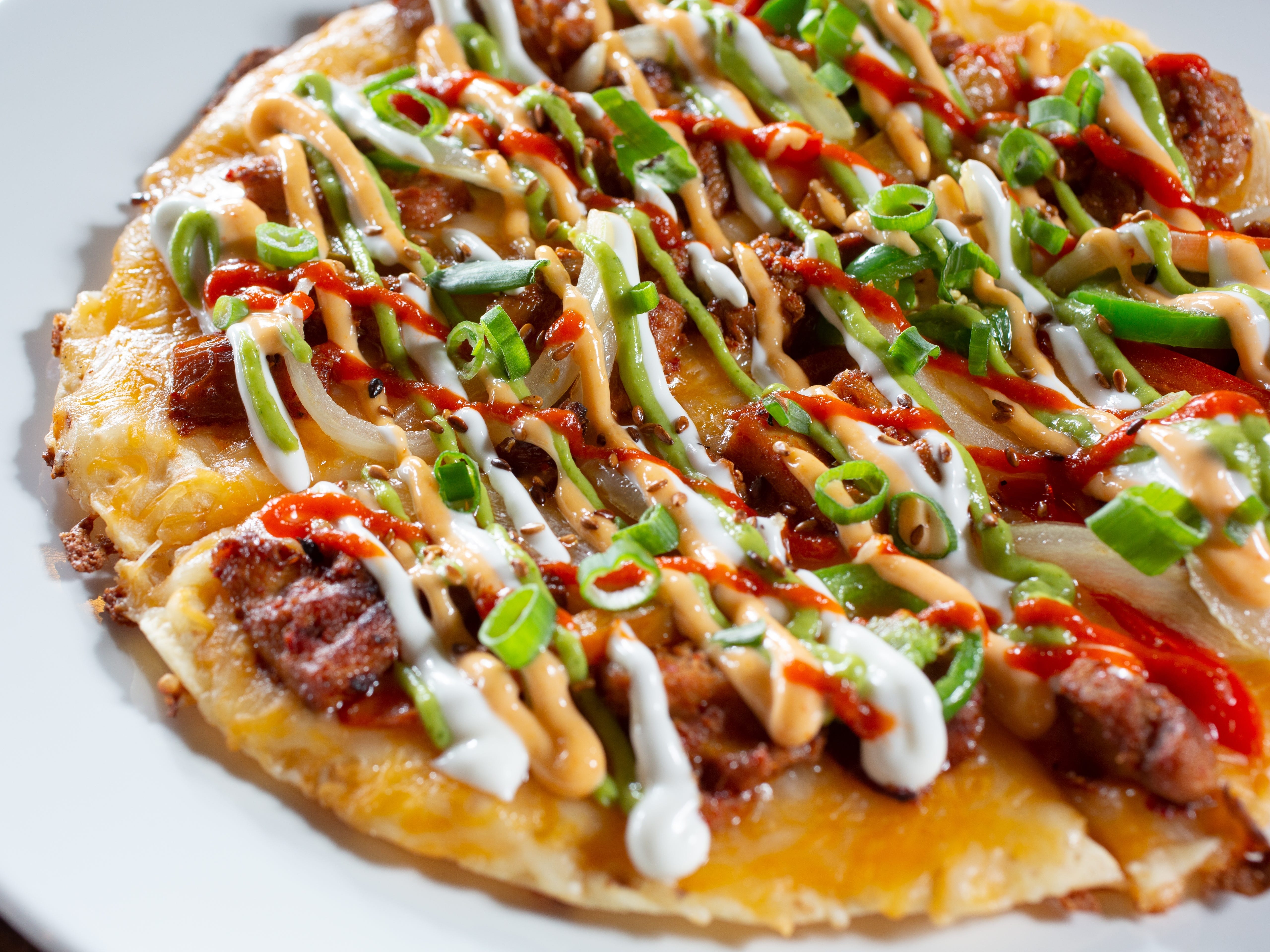 A Mexican-style pizza with lots of toppings and sauces, including green onions.