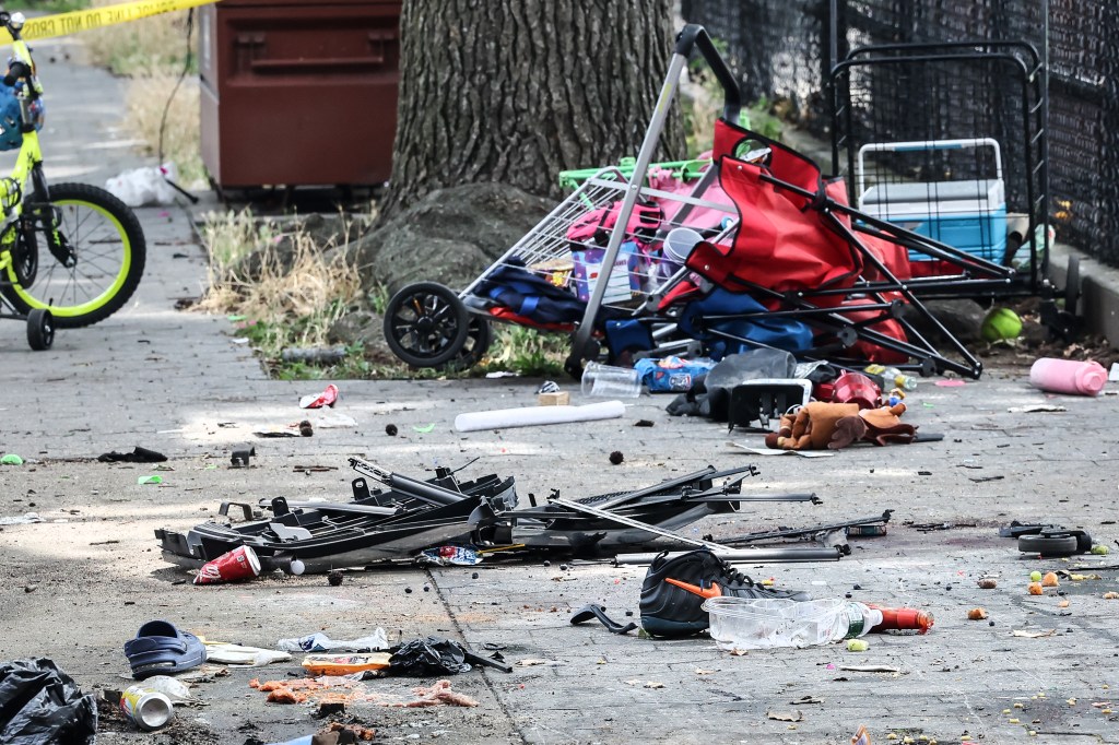 Debris from a 4th of July fatal MVA scattered across the ground, with a shopping cart, red folding chairs, a blue cooler, and a yellow bicycle visible near a tree.