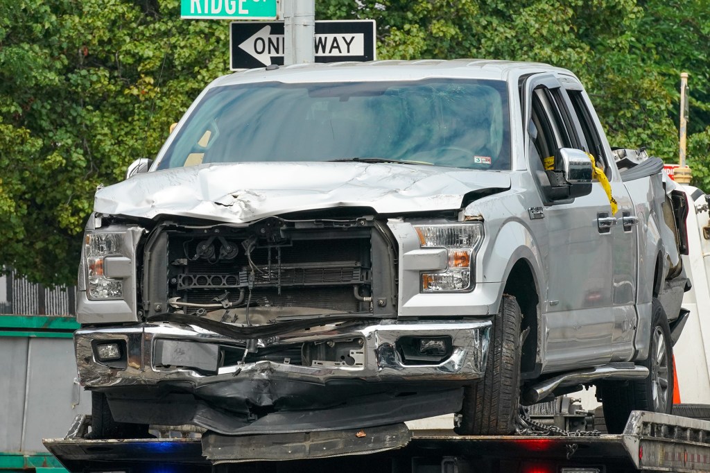 A silver Ford pickup truck with significant front-end damage, being towed on a flatbed.