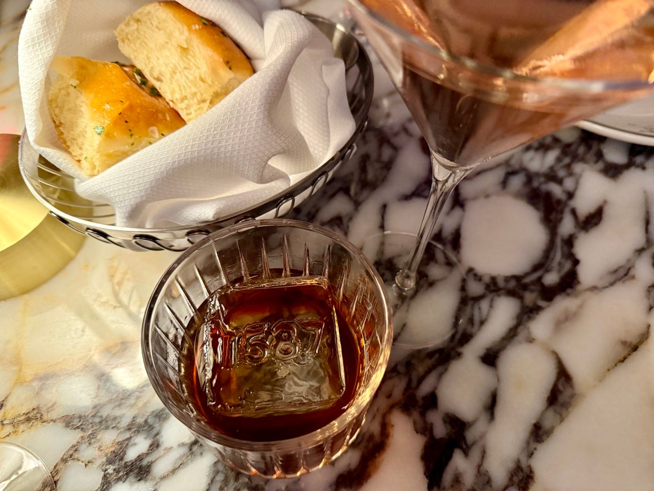 Bread basket next to drink with 1587 ice cube in it