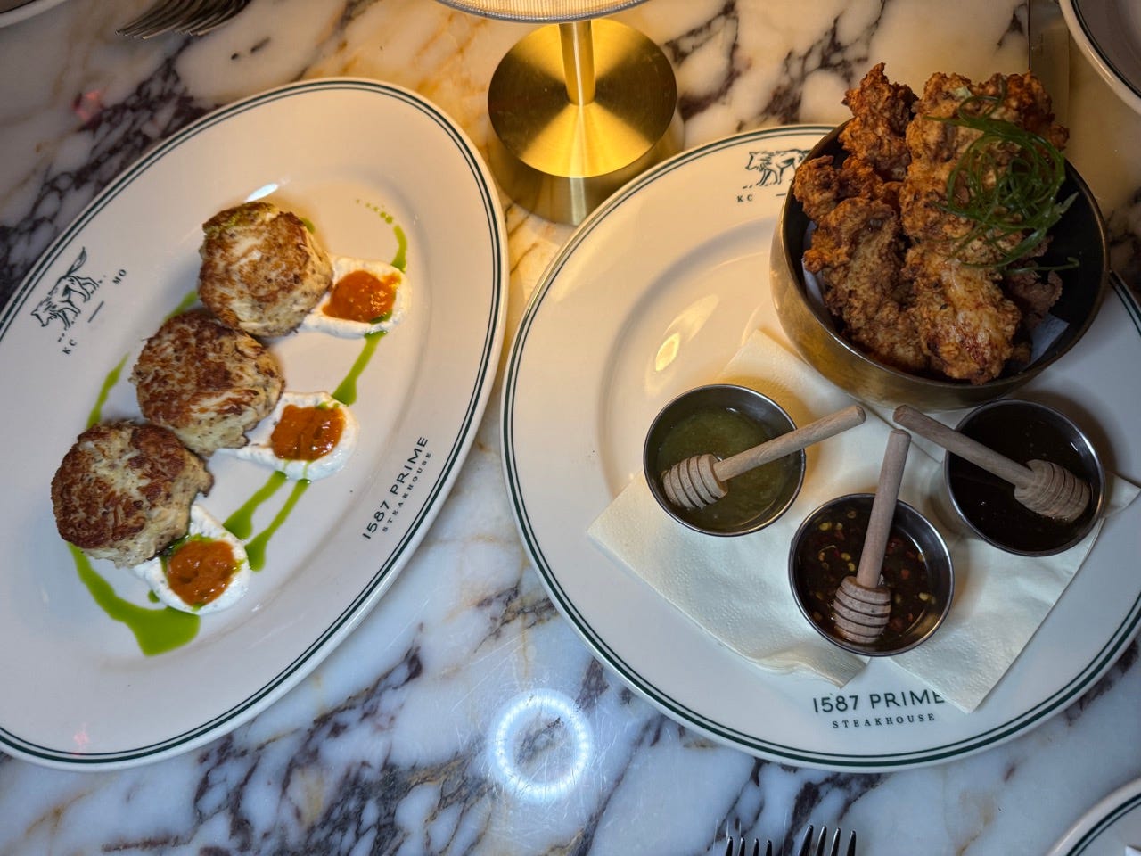 Crab cakes on plate next to plate with chicken, sauces at 1587