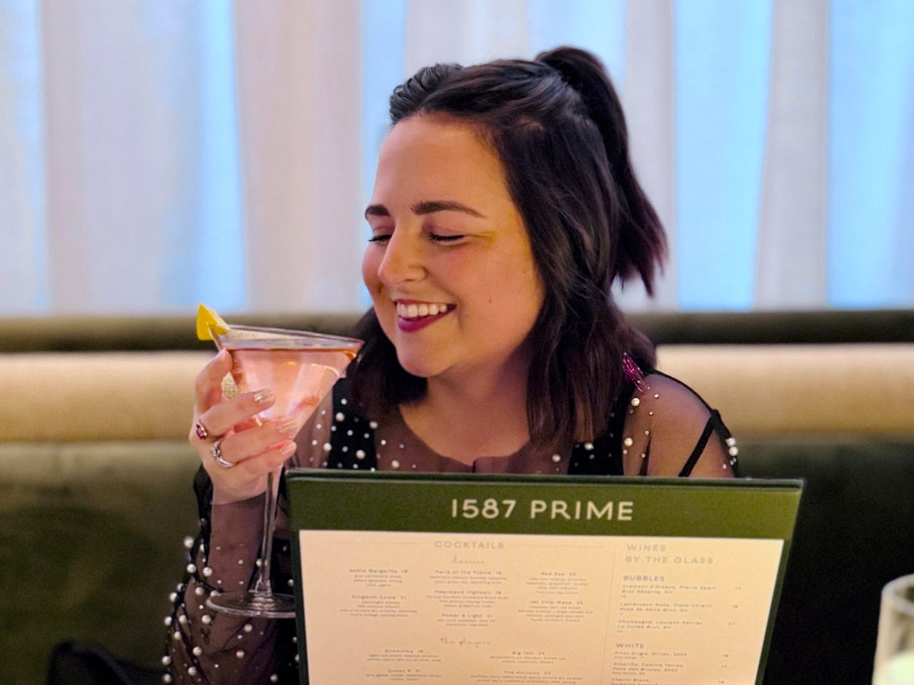 Author Kelsey Huson smiling with 1587 prime menu and The Alchemy cocktail