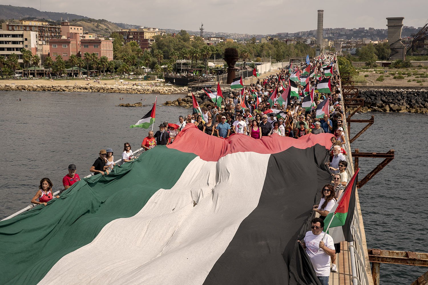 People unfurl a giant bridge-width Palestinian flag as others hold flags on sticks filling a bridge to the horizon.