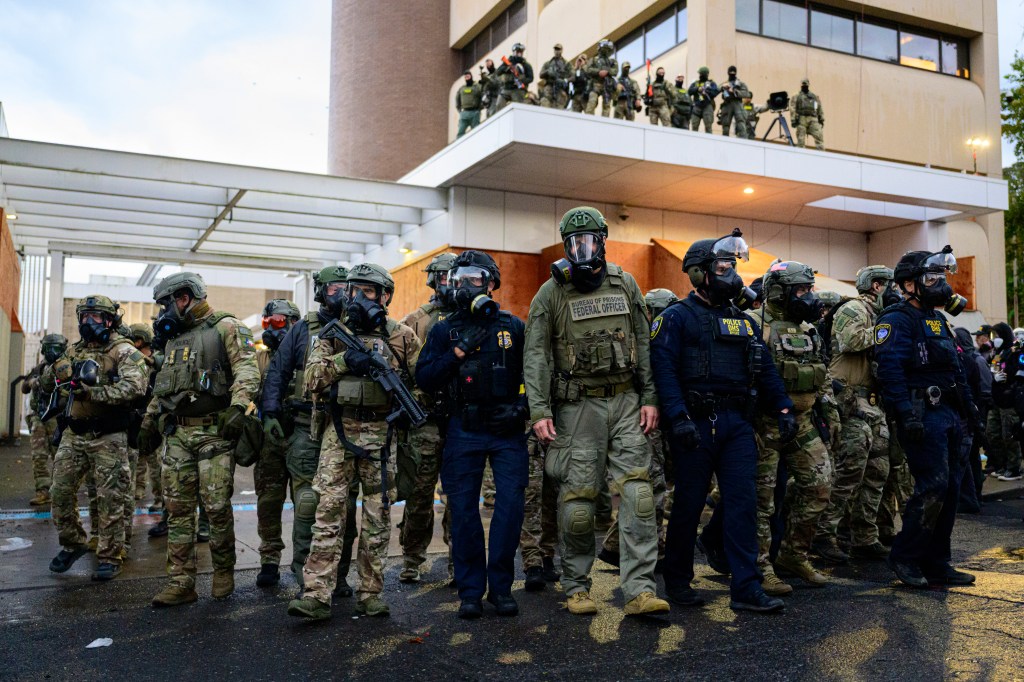 Federal agents in riot gear and gas masks confront anti-I.C.E. protesters.