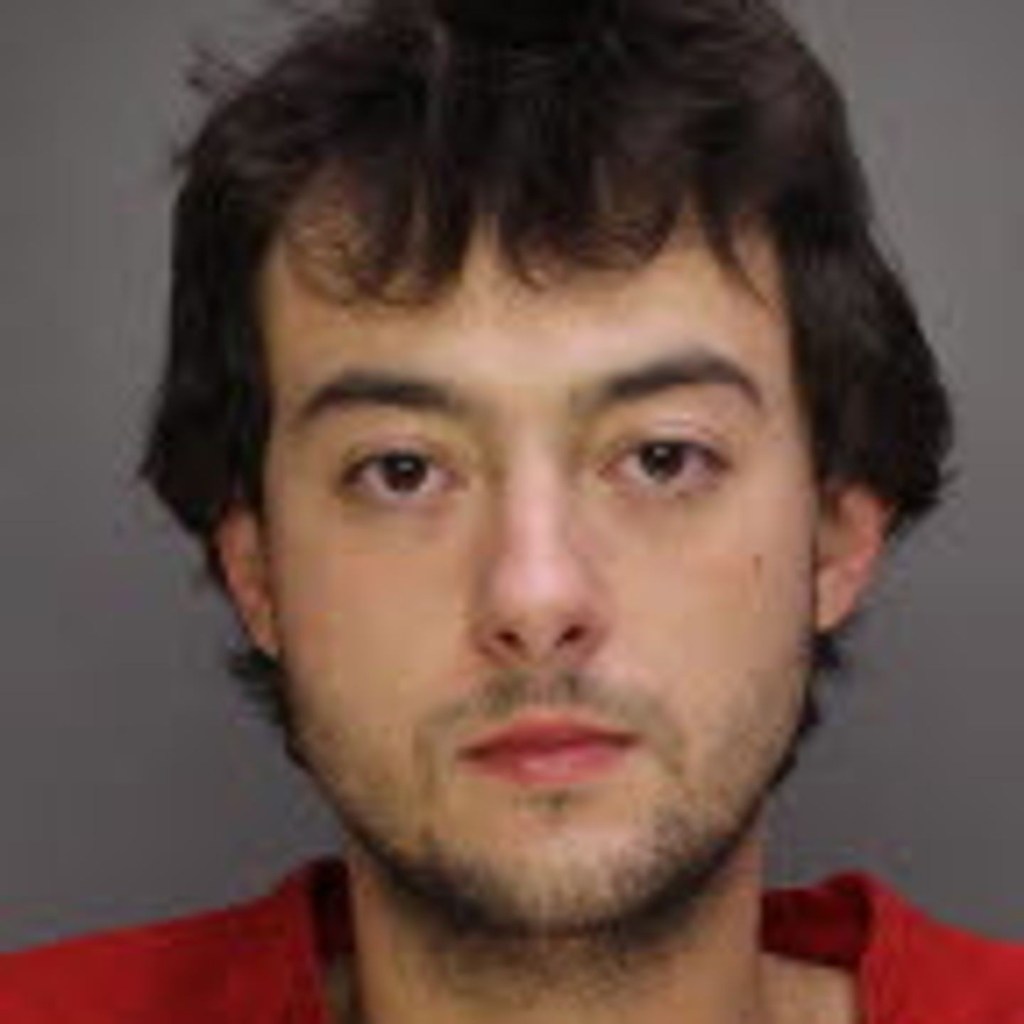 Mugshot of a man with dark hair and stubble, wearing a red shirt.