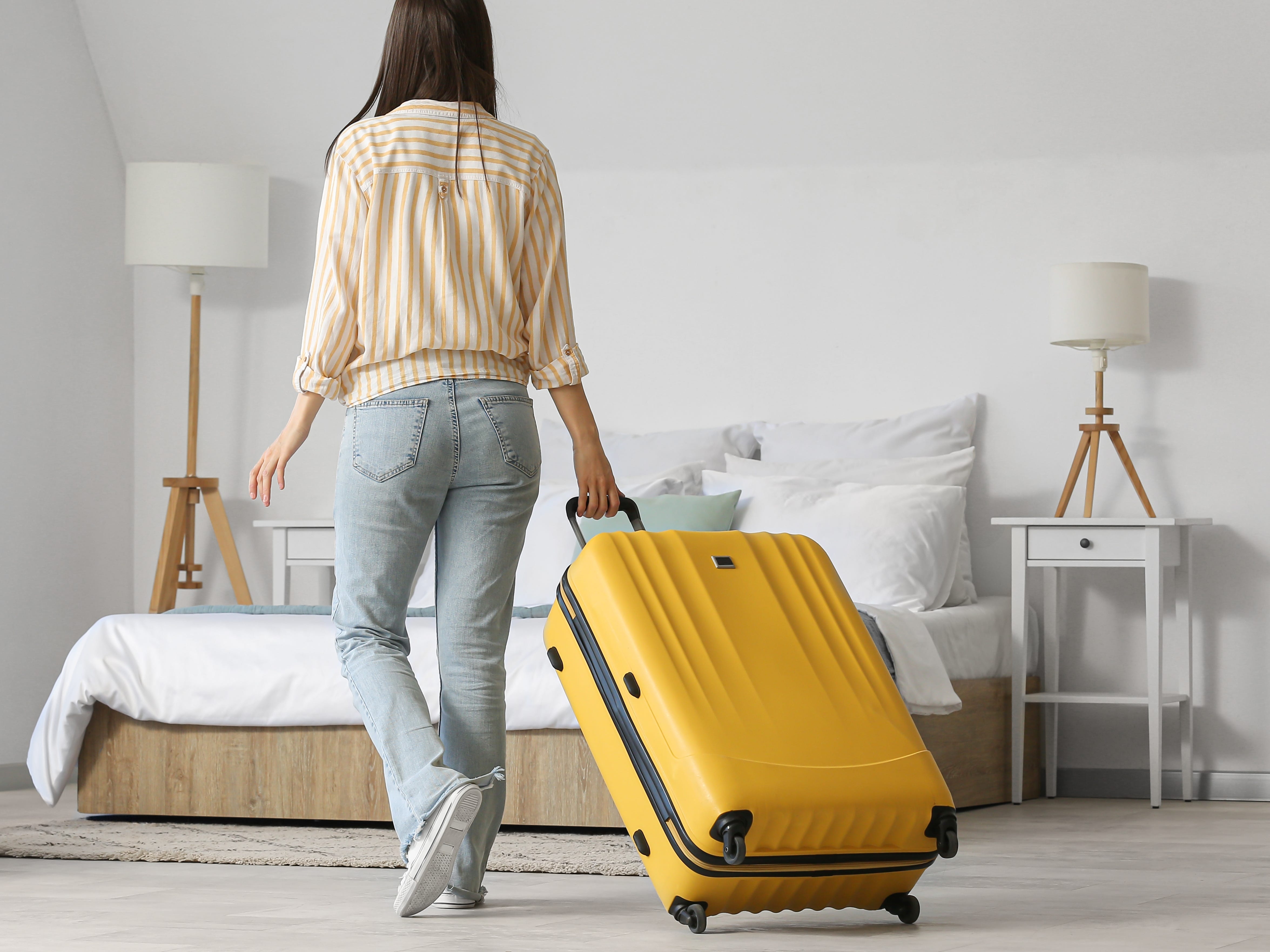 A girl rolling a yellow suitcase in a bedroom.