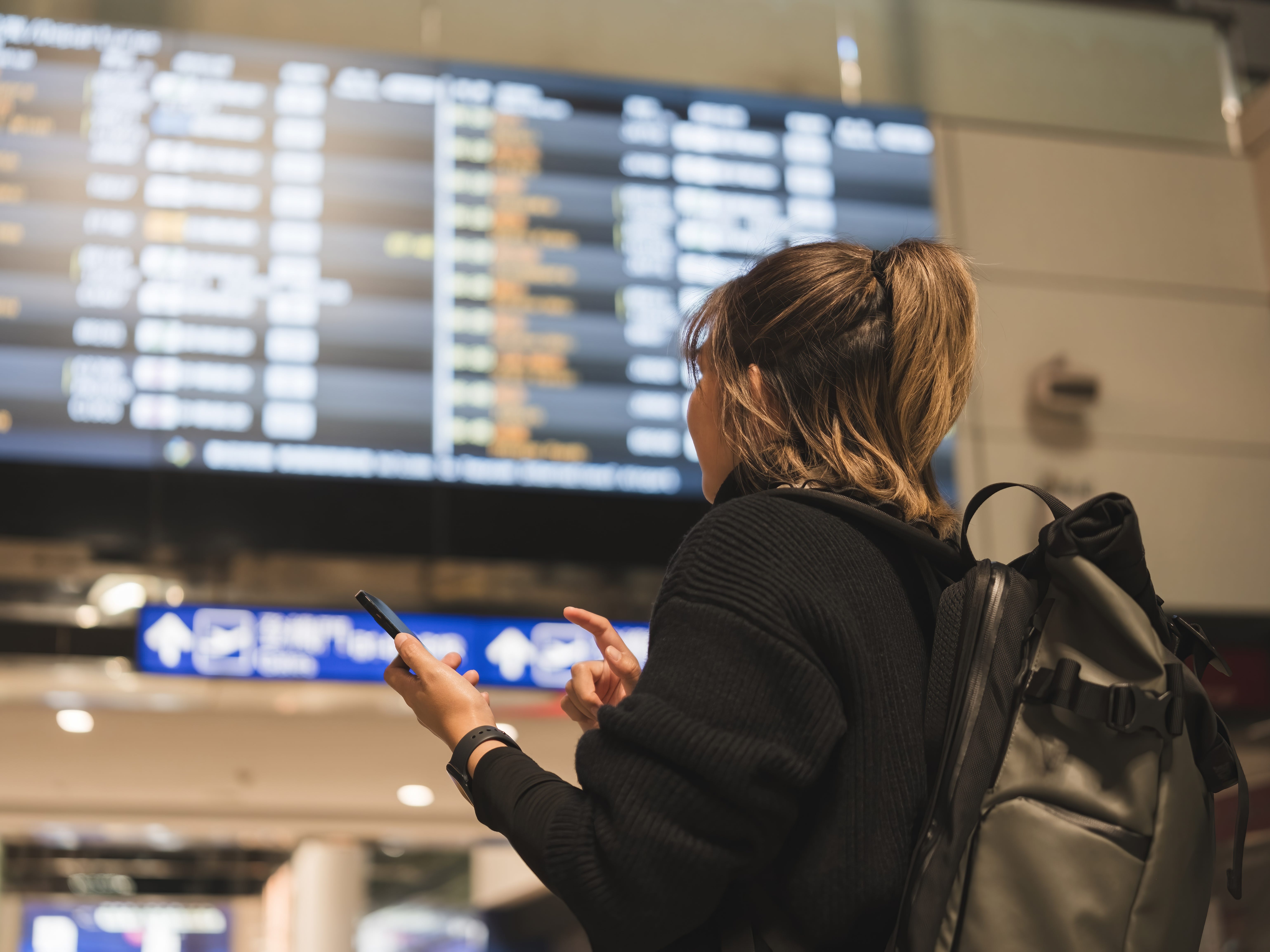 A woman turned away from the camera, on her phone looking at a screen of flight times.
