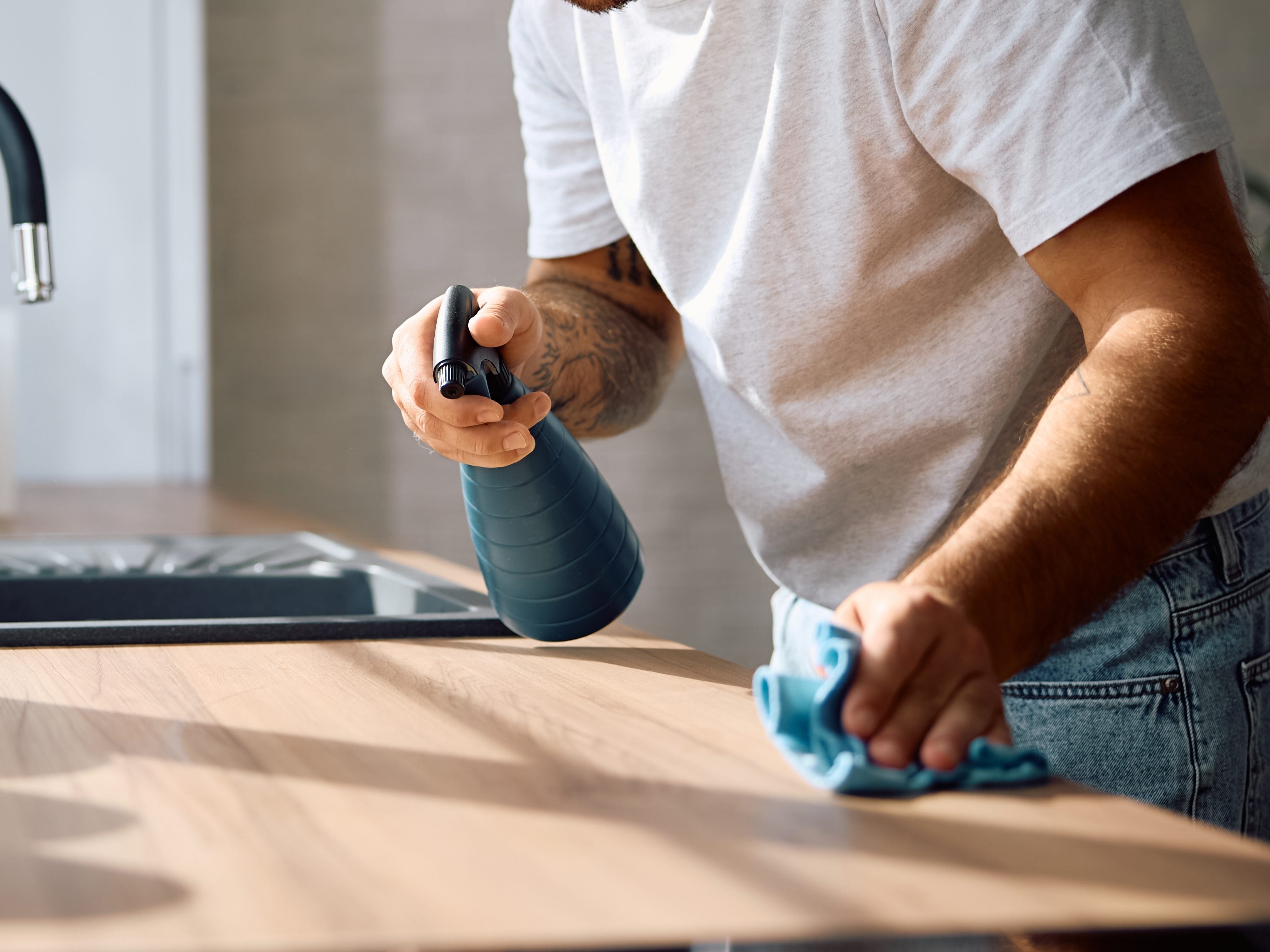 A person spraying cleaning liquid on a kitchen counter.