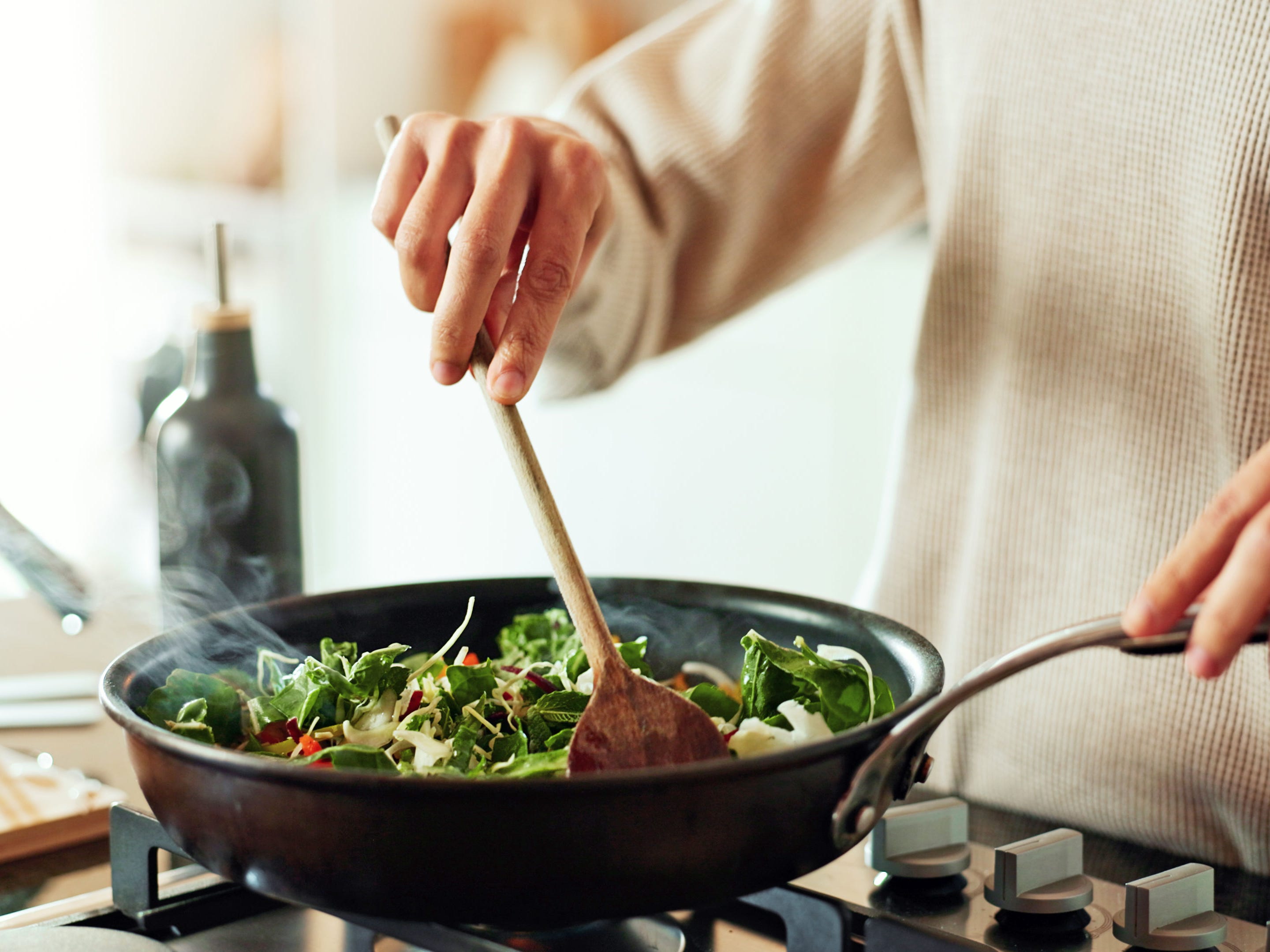 A person stirring vegetables in a pan on a stovetop.