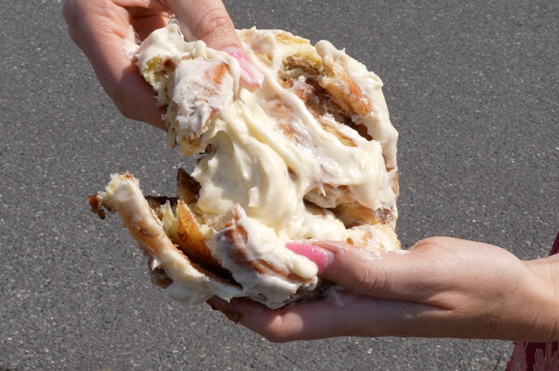 Cinnamon bun covered in icing being pulled apart