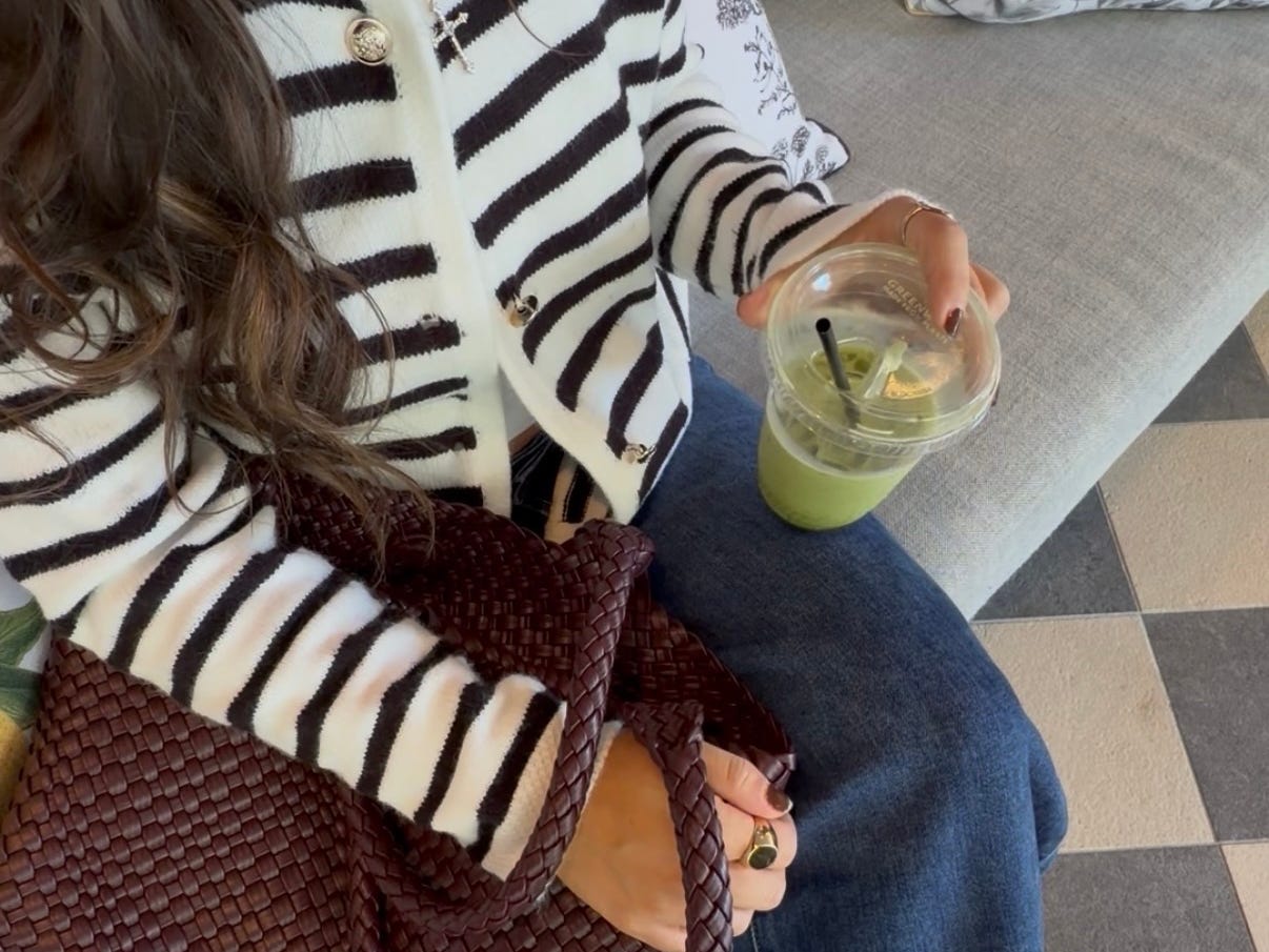 A close-up of Amanda wearing a striped sweater, blue jeans, carrying matcha and a maroon bag.