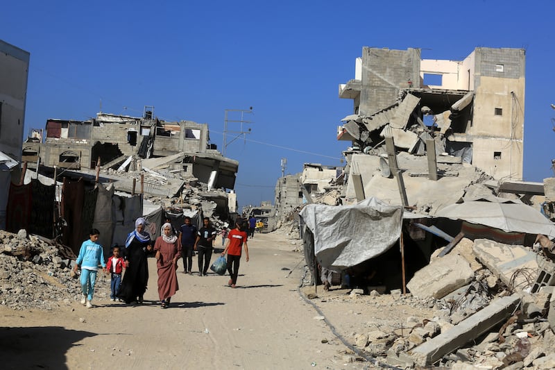 Palestinians walk among the rubble of destroyed buildings in Khan Yunis, Gaza on October 21, 2025.