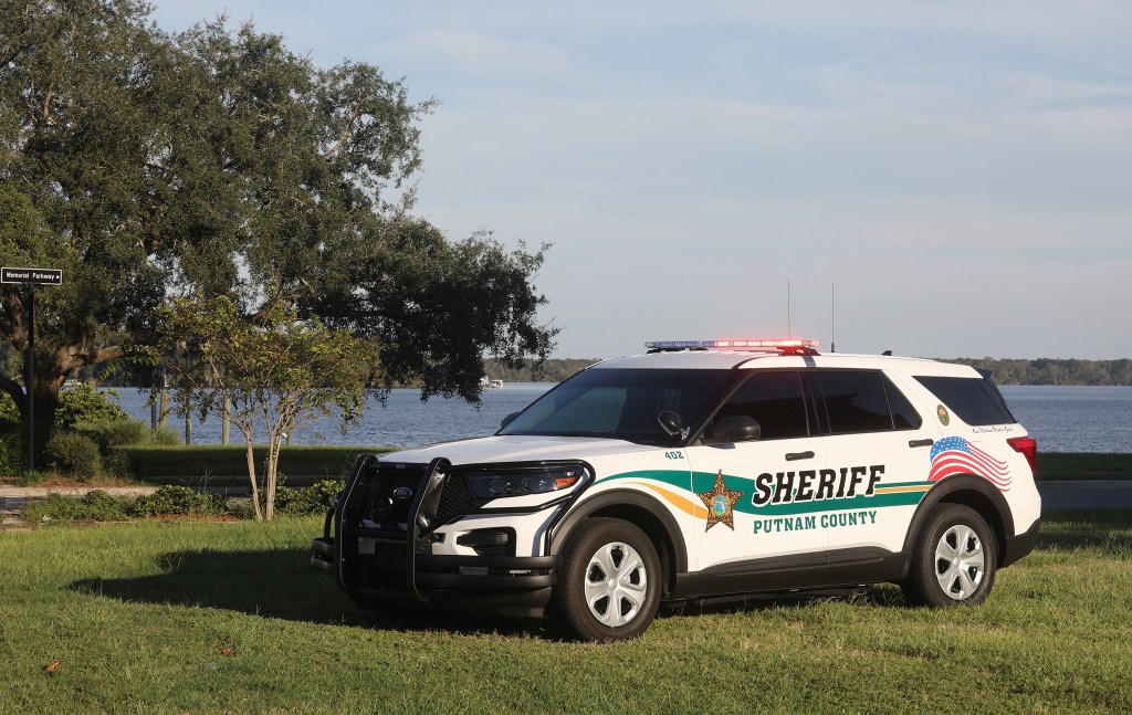 White and green Putnam County Sheriff's patrol car parked on grass near a lake.