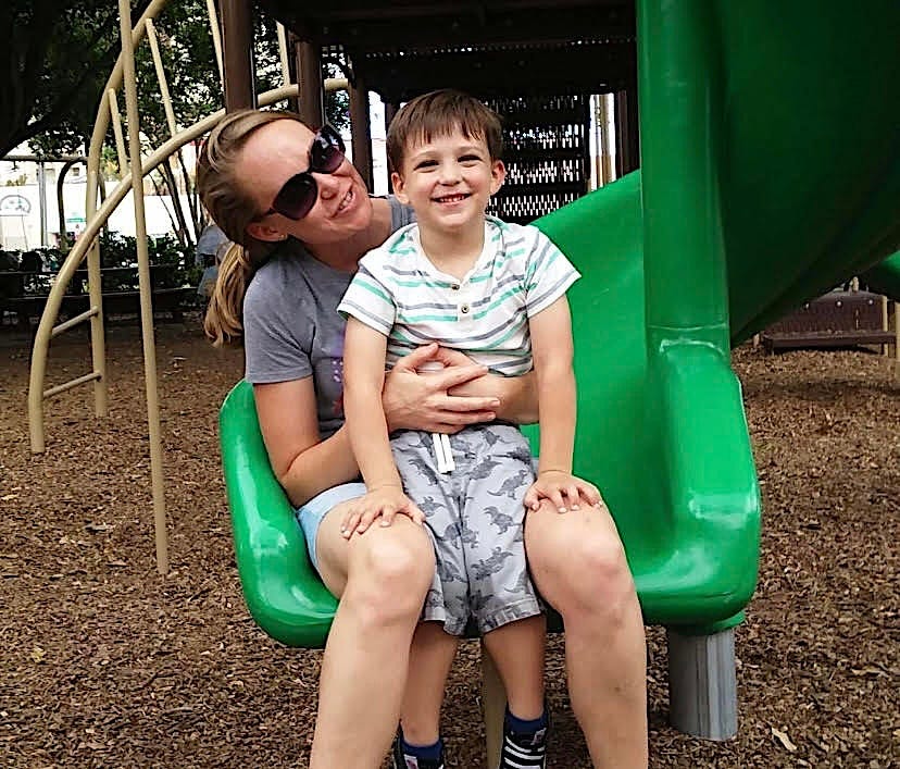 The author with her son at the park, sitting on a green slide, when he was 3 years old.