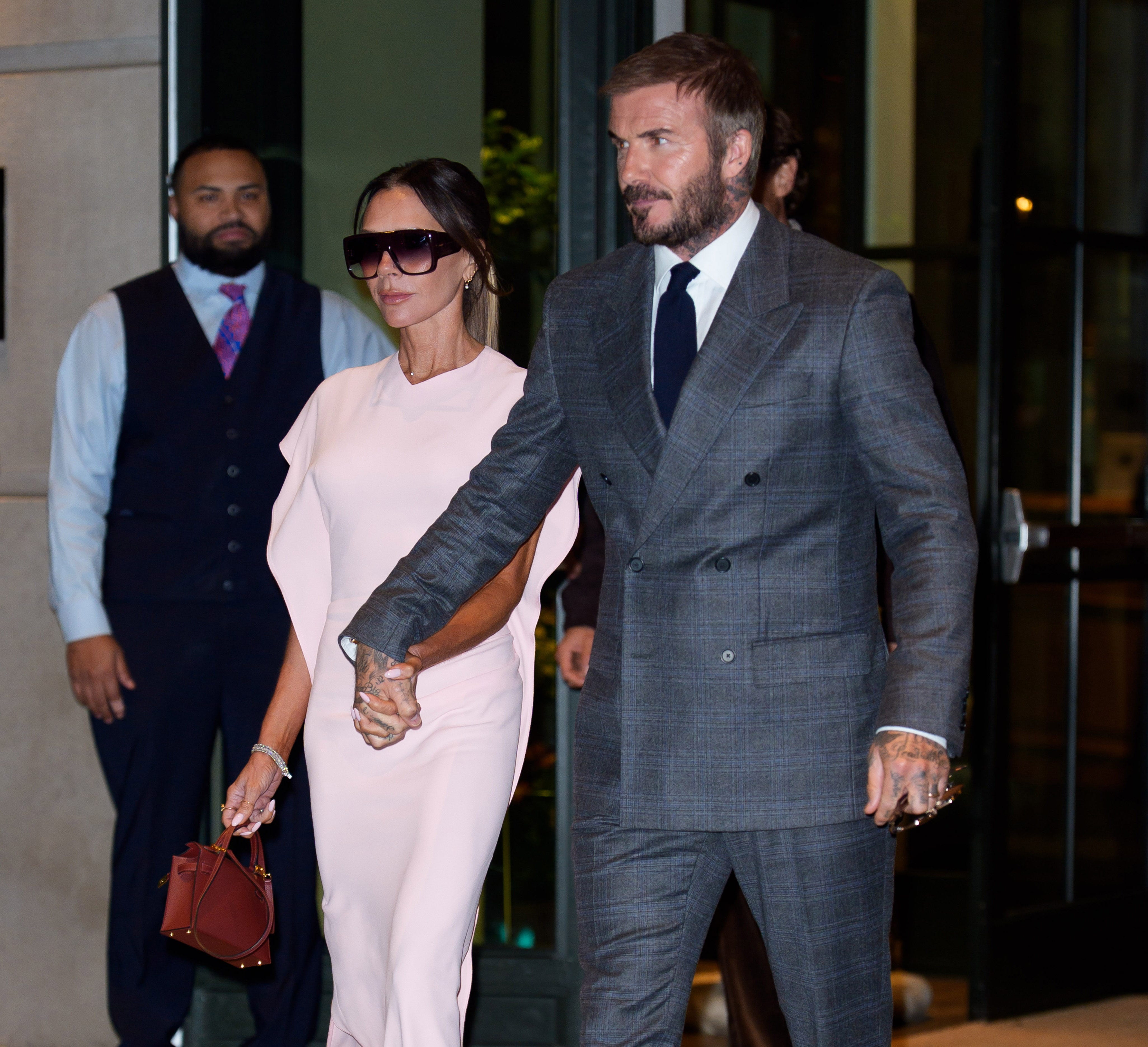 Victoria Beckham in sunglasses holding David's hand, leaving a building