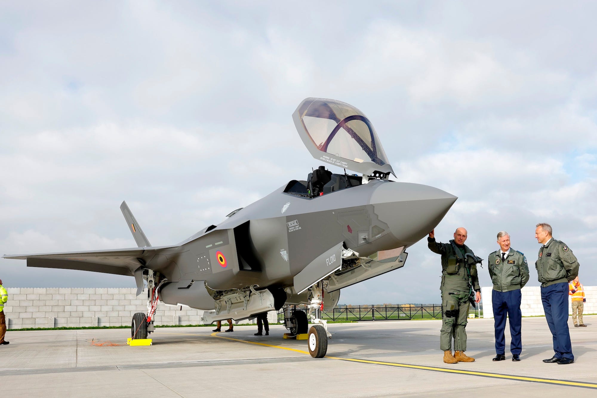 Three men stand beside a fighter jet parked on tarmac