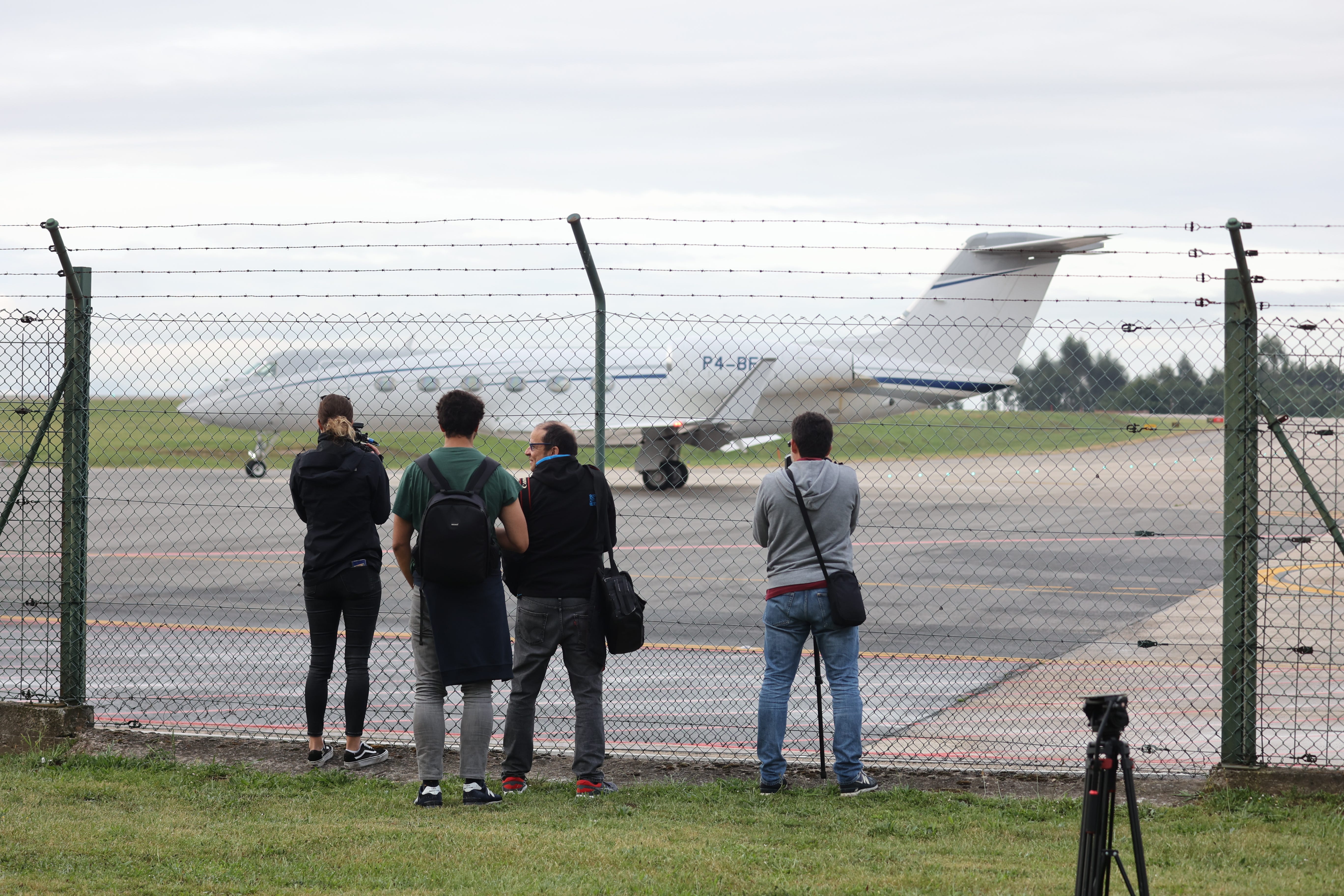 Paparazzi standing outside the fence of a private terminal, taking photos of a private jet.