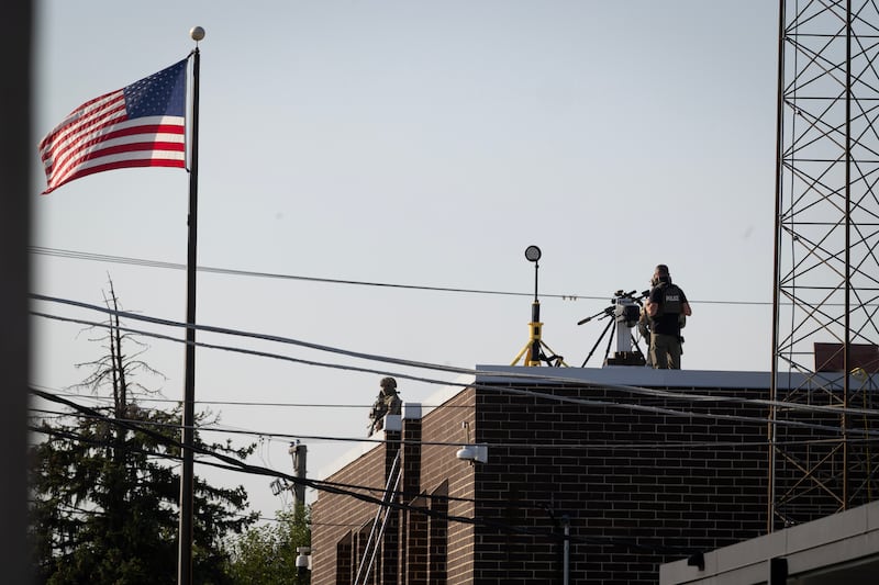 A federal law enforcement stands next to a sniper rifle on the roof of an immigrant processing and detention center during a protest