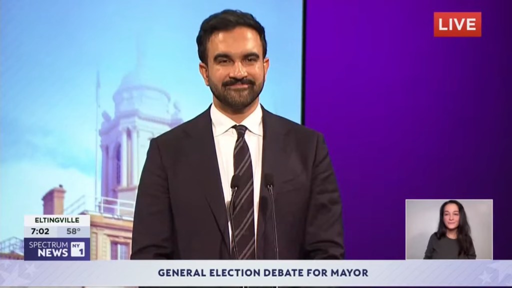 Zohran Mamdani at a mayoral debate, with a small box displaying a sign language interpreter.