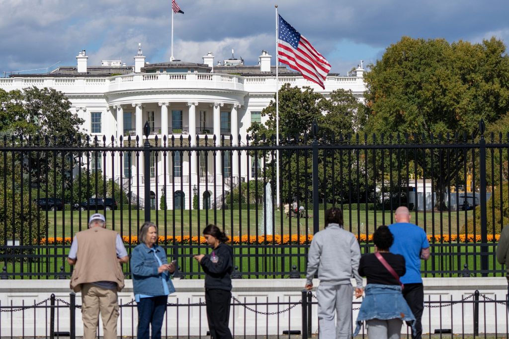 The White House East Wing with an American flag flying, as people look on.
