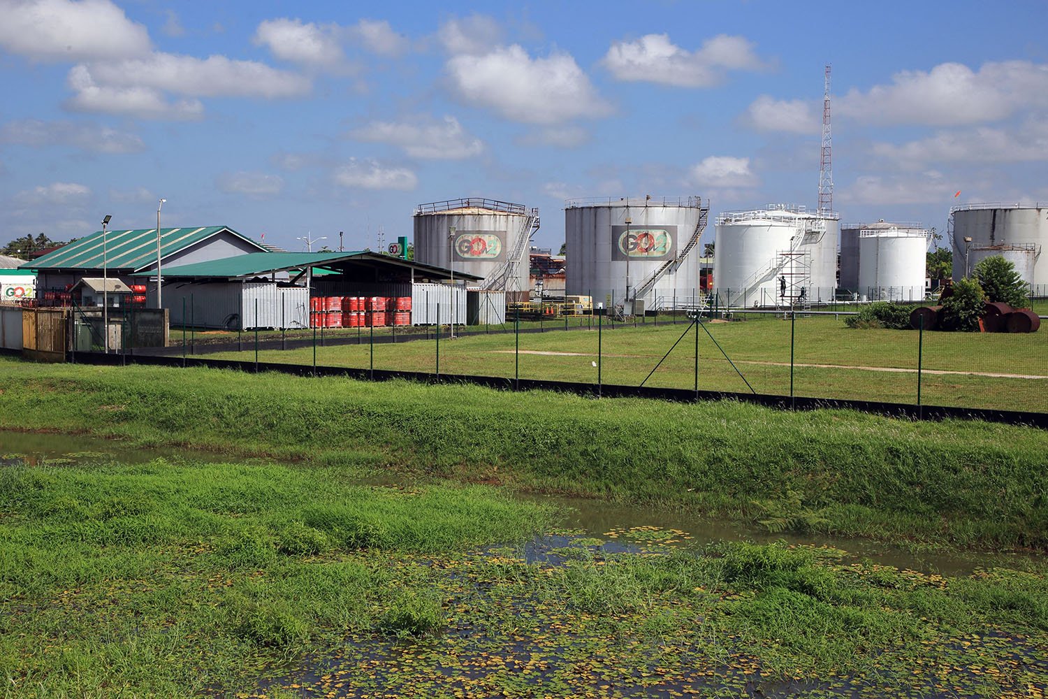 Green grass and fuel tanks sit on the horizon against a blue sky.
