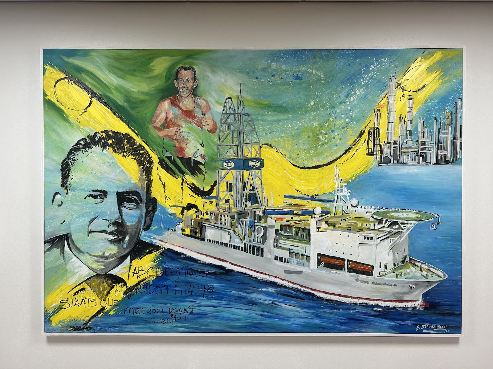 A mural depicts a man's face atop a green, yellow, and blue background. In the foreground of the image, an oil-drilling boat floats on blue water.
