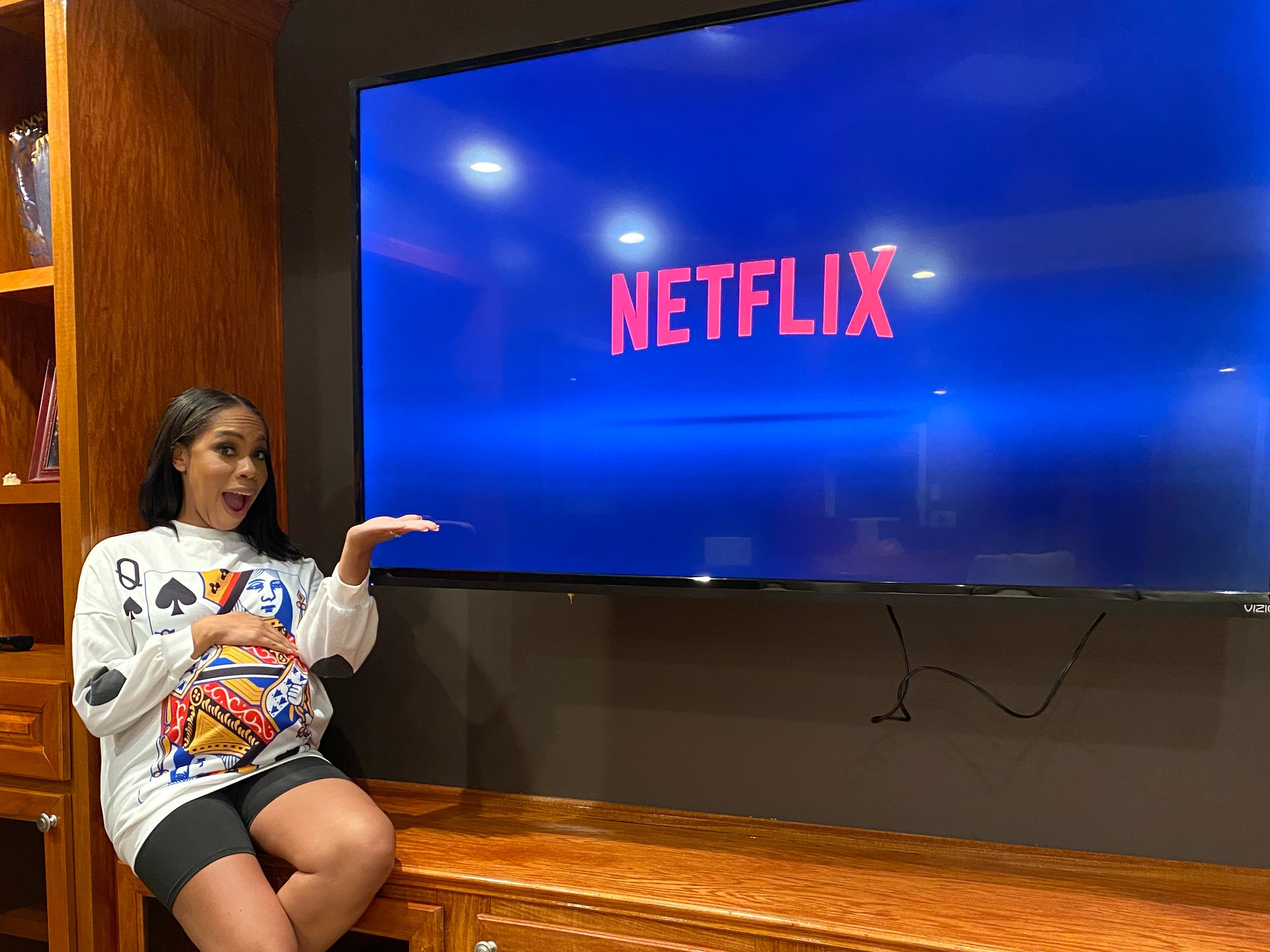 A pregnant woman sitting next to a giant TV screen showing Netflix
