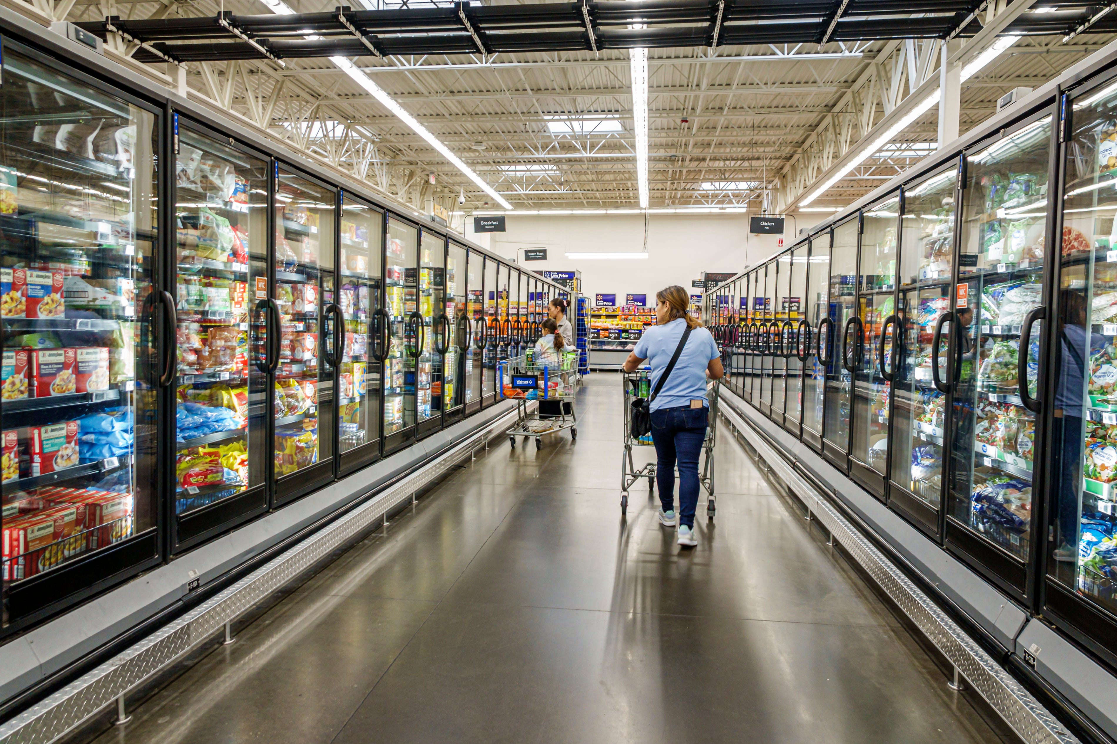 Walmart Supercenter, frozen foods aisle glass door freezers, women shoppers adults pushing carts.